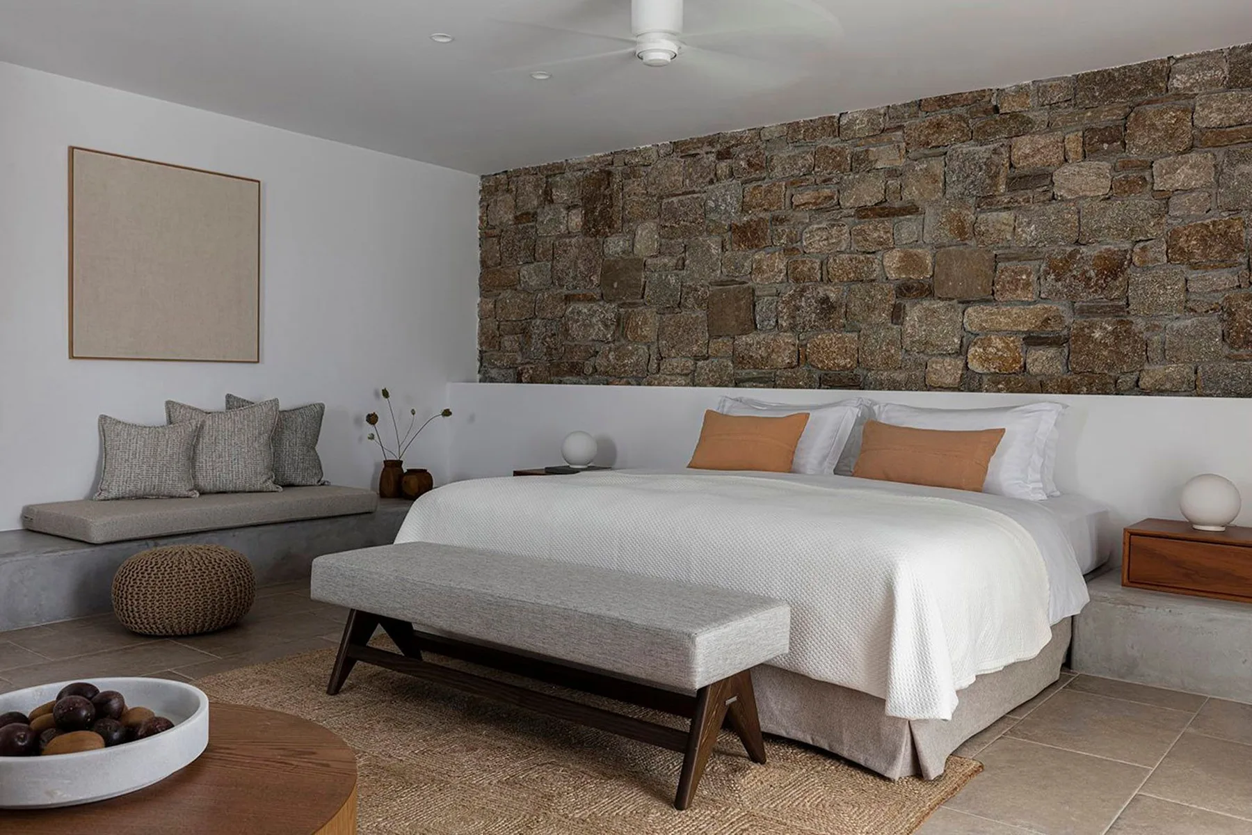 A bedroom with a bed, a stone accent wall, and a small seating area.