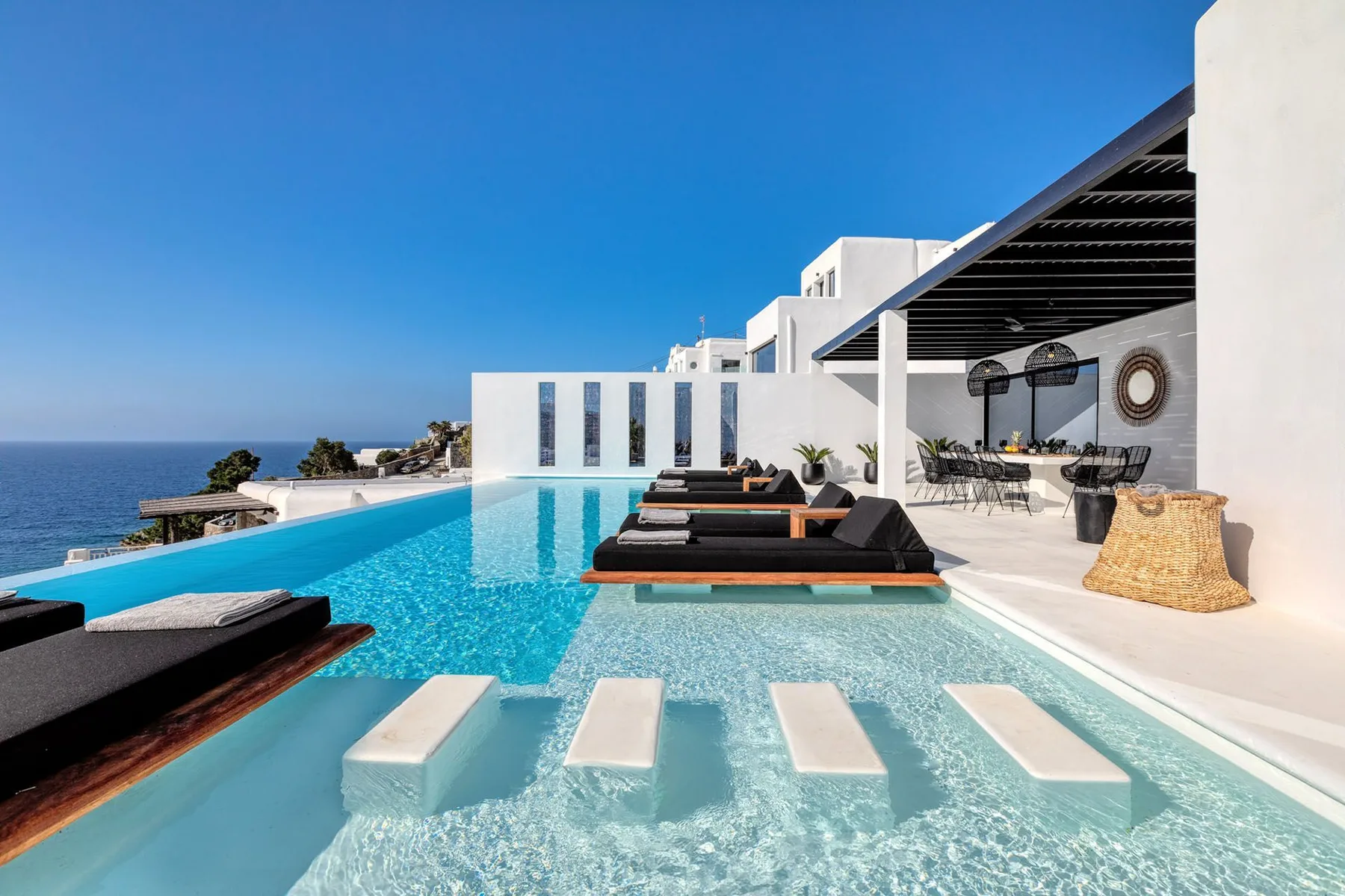 An outdoor pool beside a modern white building, with the sea visible beyond.