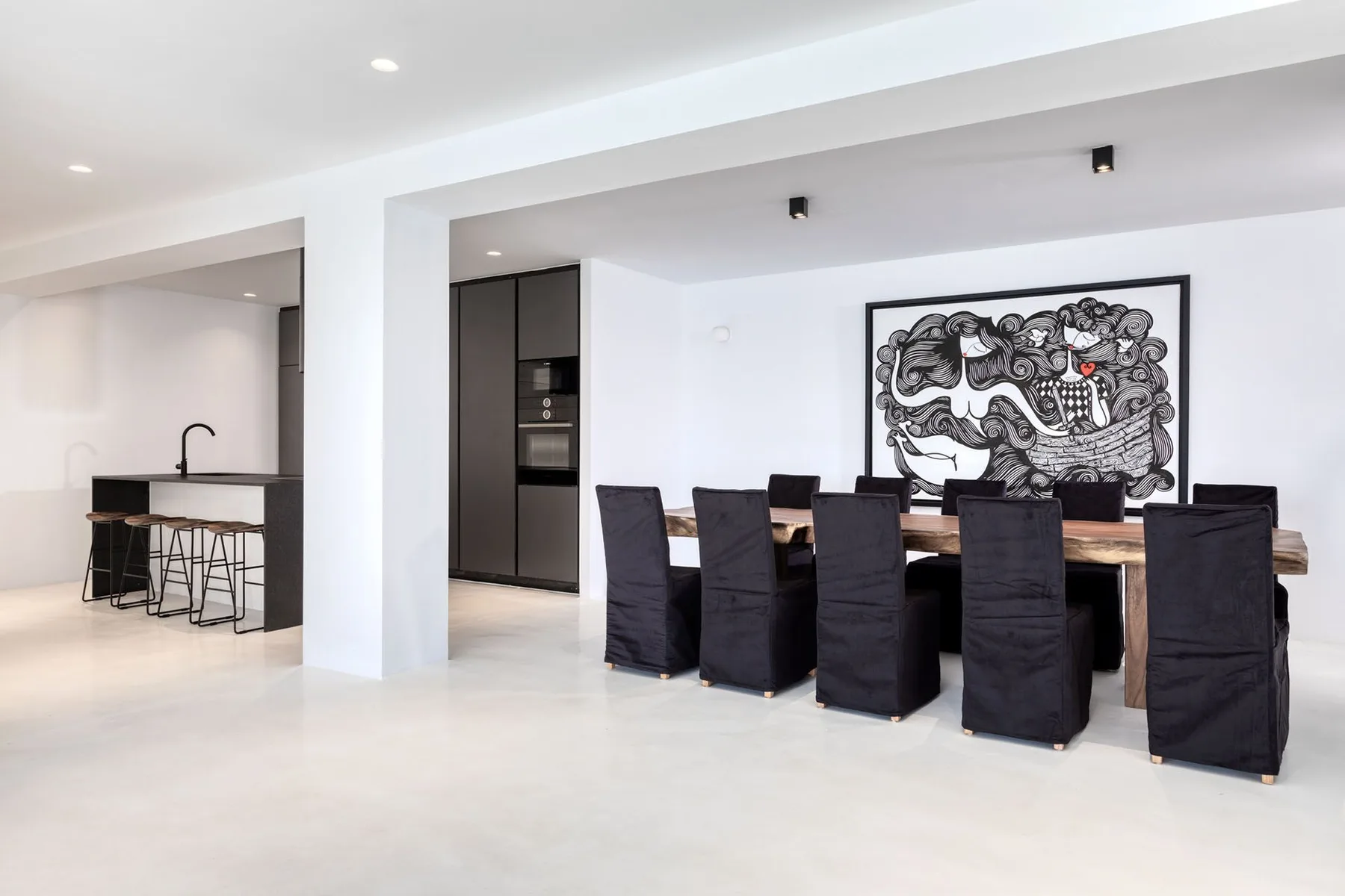 A dining area with a long table and dark-covered seating beneath a large artwork.