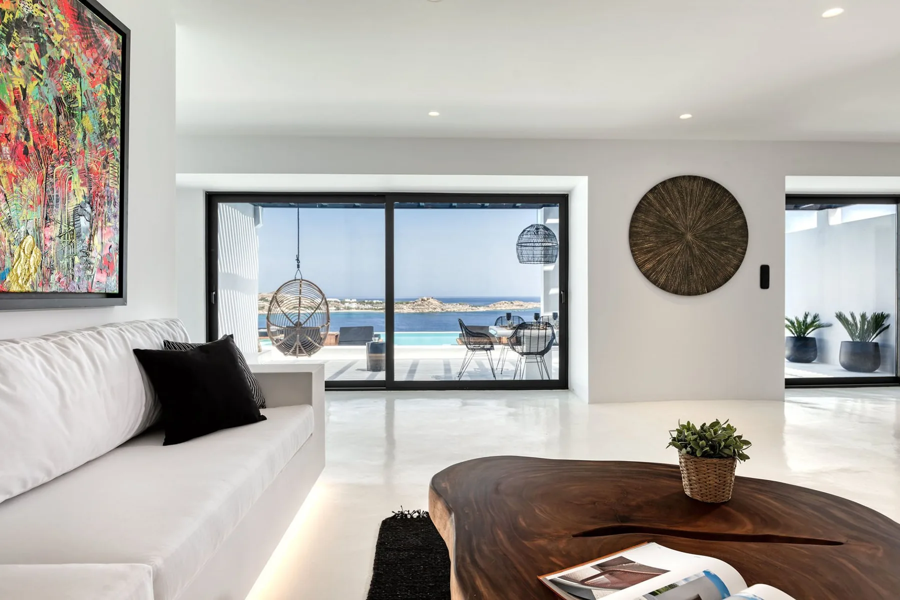 Bright living room with white seating, a low wooden table, and large windows overlooking the water.
