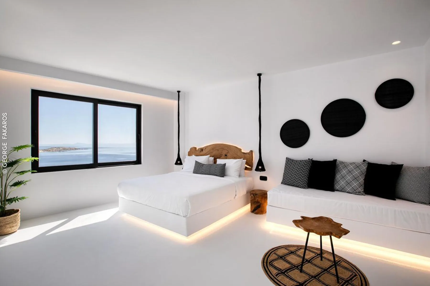 A bright bedroom with a bed, built-in seating, and a wide window overlooking the water.