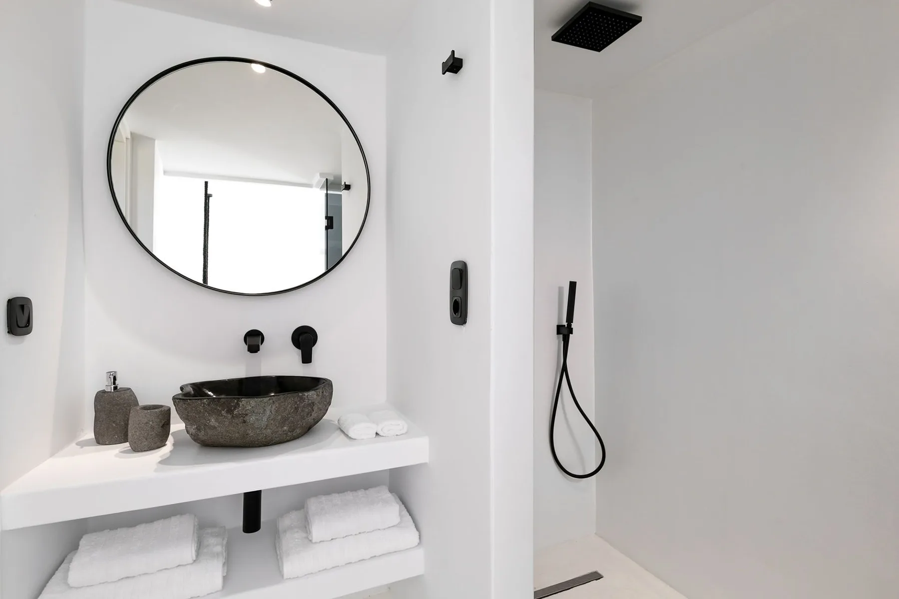 A bright bathroom vanity with a round mirror and an open shower area.