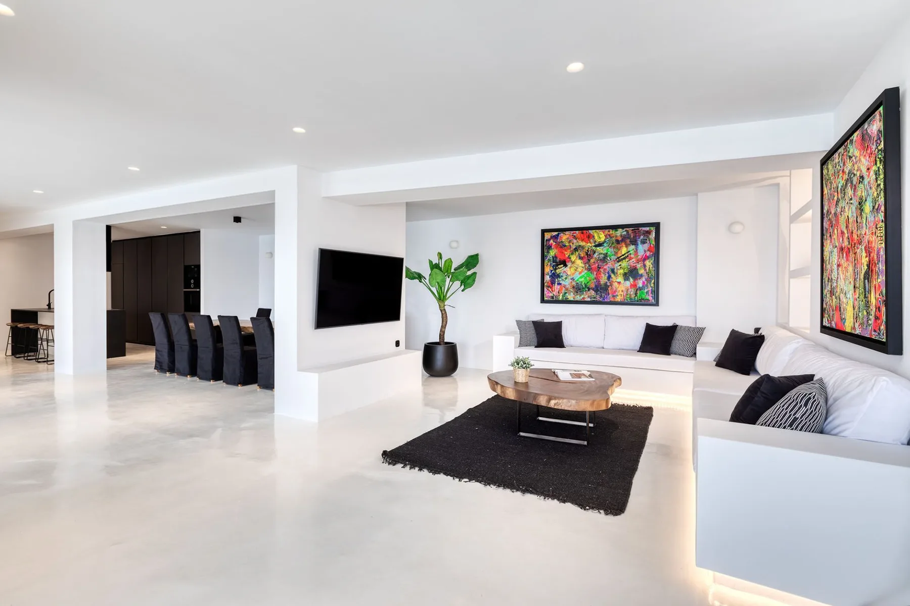 A bright open-plan living room has a seating area, coffee table, and colorful wall art.
