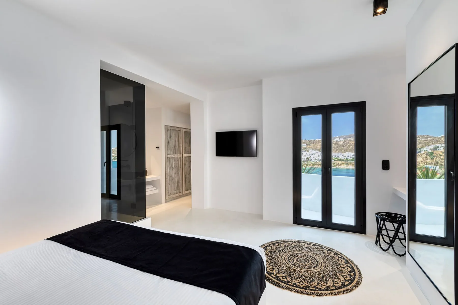 A bright bedroom with a bed, wall-mounted television, and glass doors overlooking a pool.
