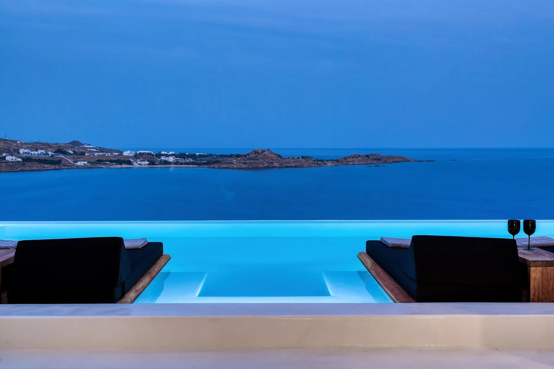 An infinity pool overlooks the sea, with dark seating beside the water.