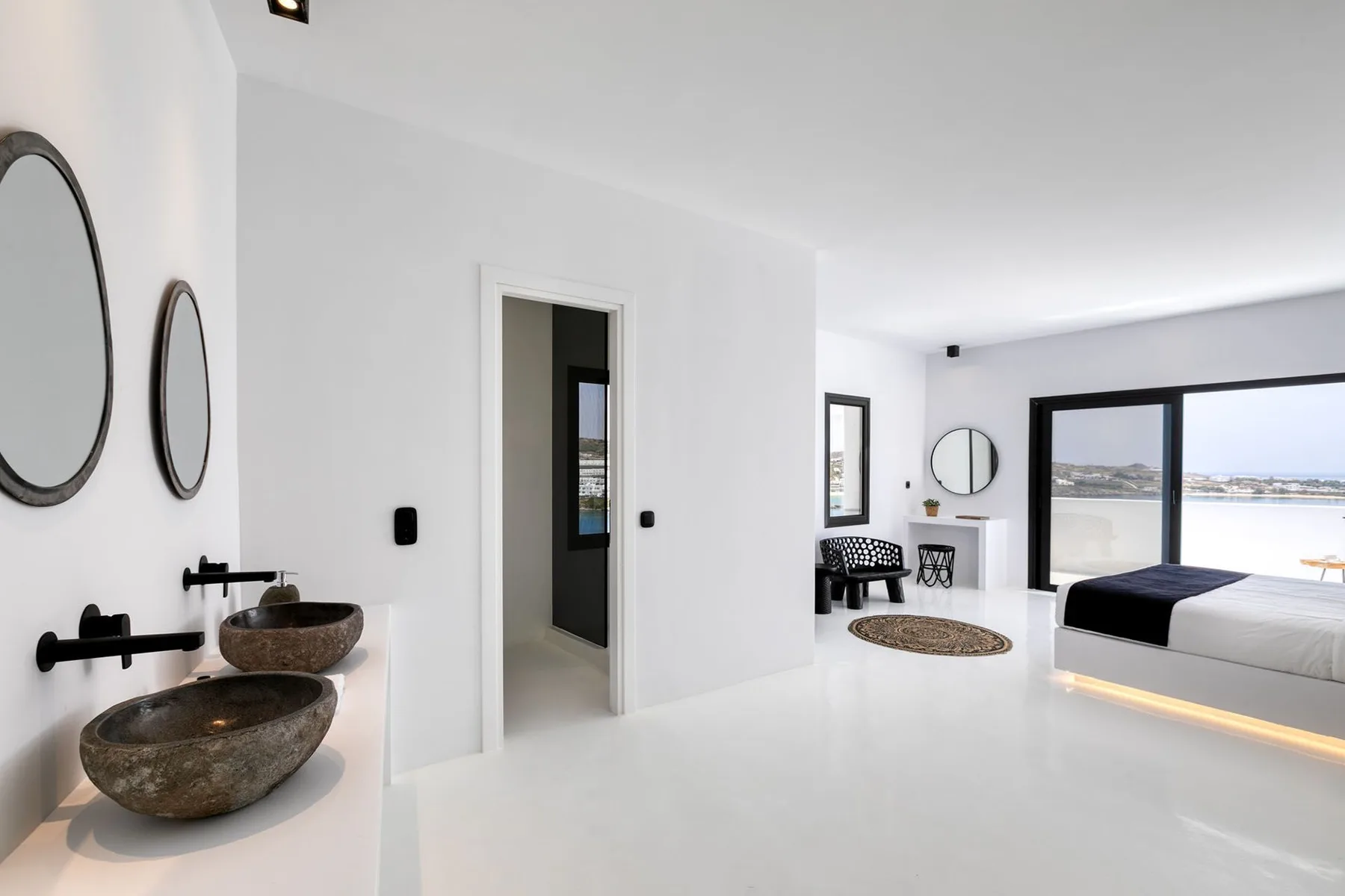 A bright bedroom with a bed beside large windows overlooking the water.