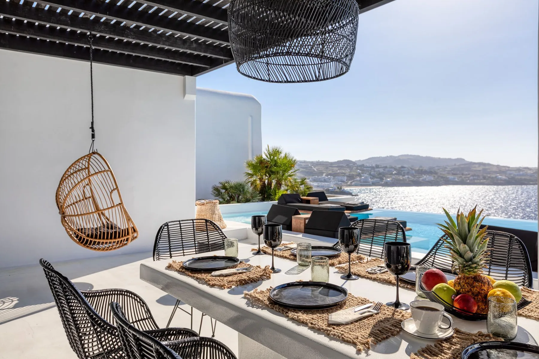 An outdoor dining area overlooks a swimming pool and the sea.