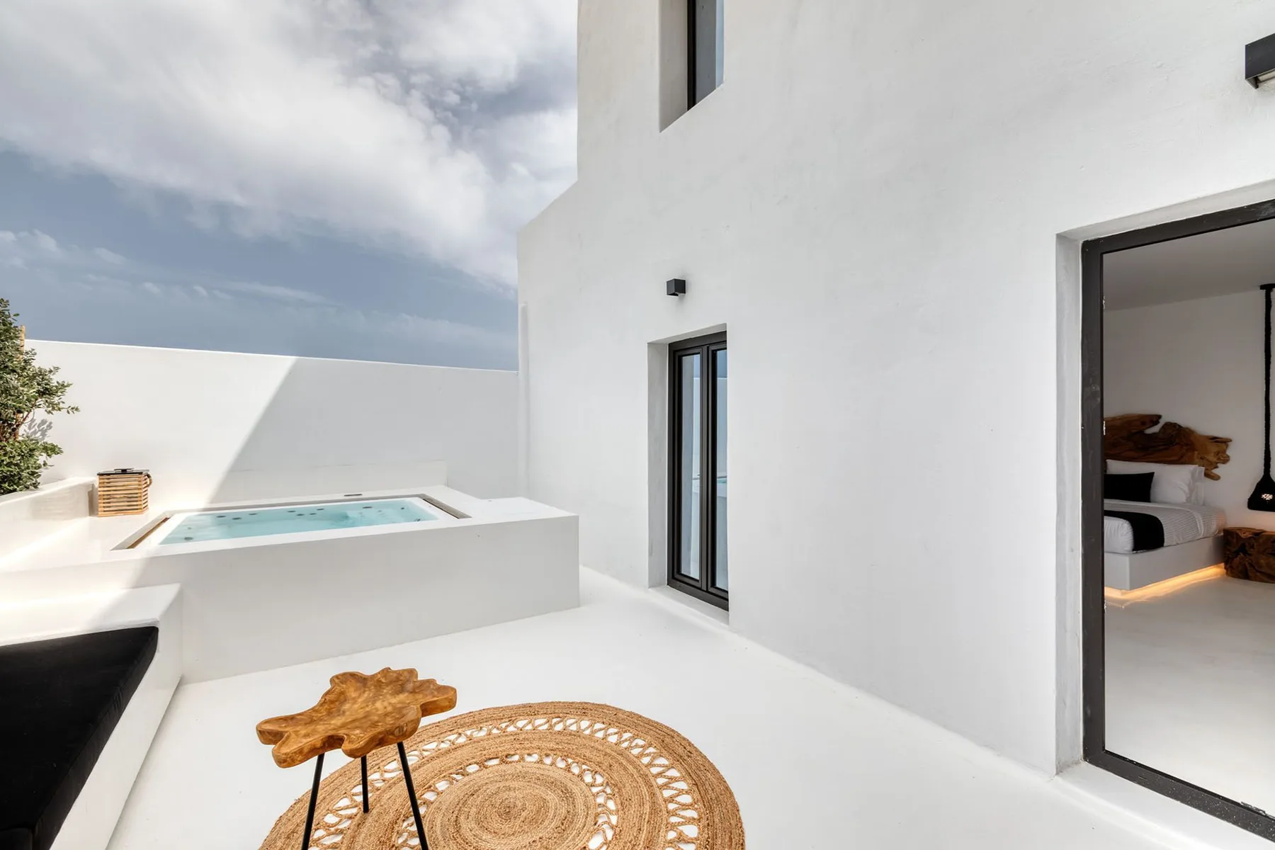 A bright white patio features a small pool and a woven outdoor rug.