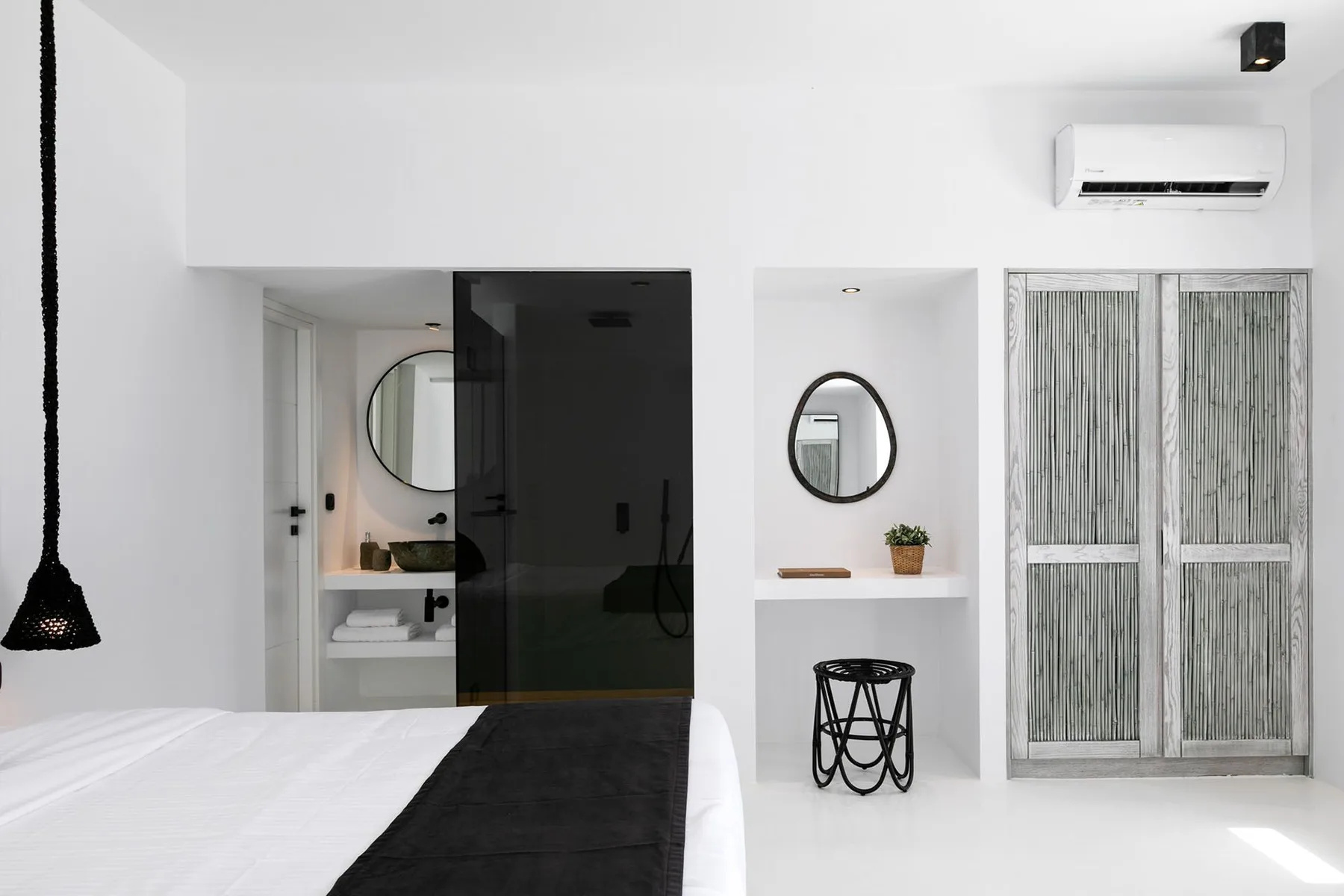 A bright bedroom with a bed beside a bathroom vanity and sliding doors.