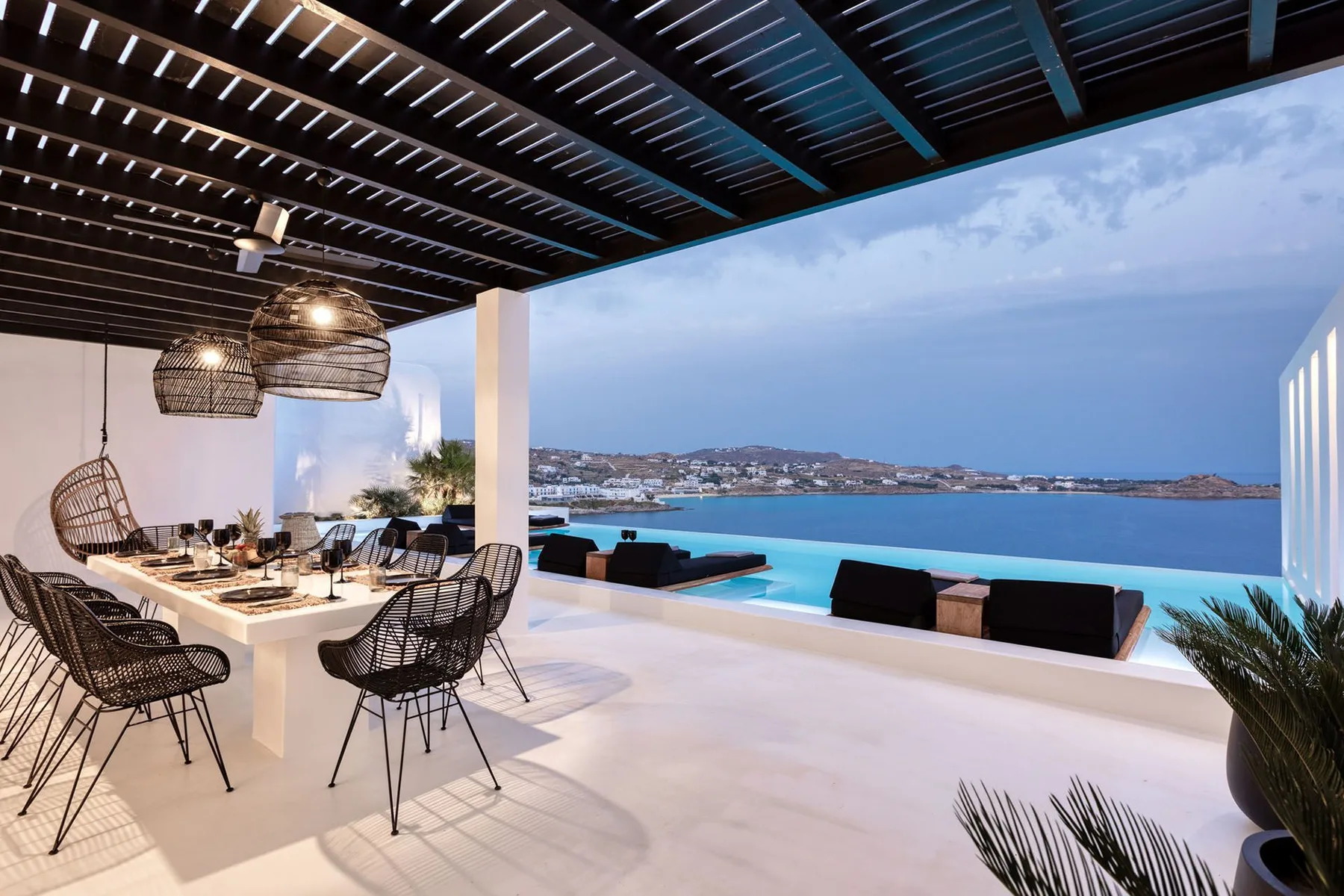 An outdoor dining area with a table and seating overlooks a swimming pool and the sea.