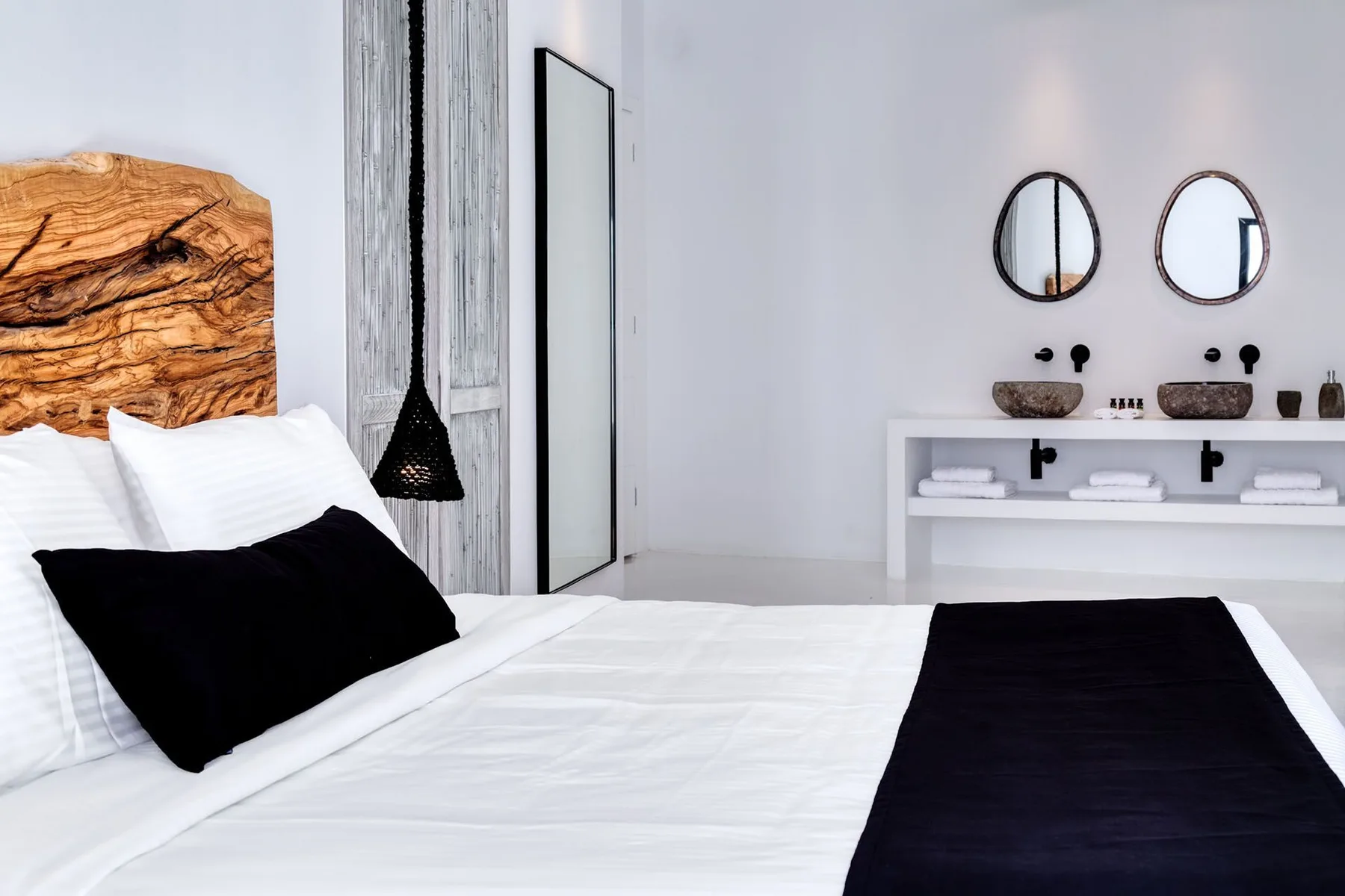 A bright bedroom with a bed, black bedding accents, and a double sink vanity.