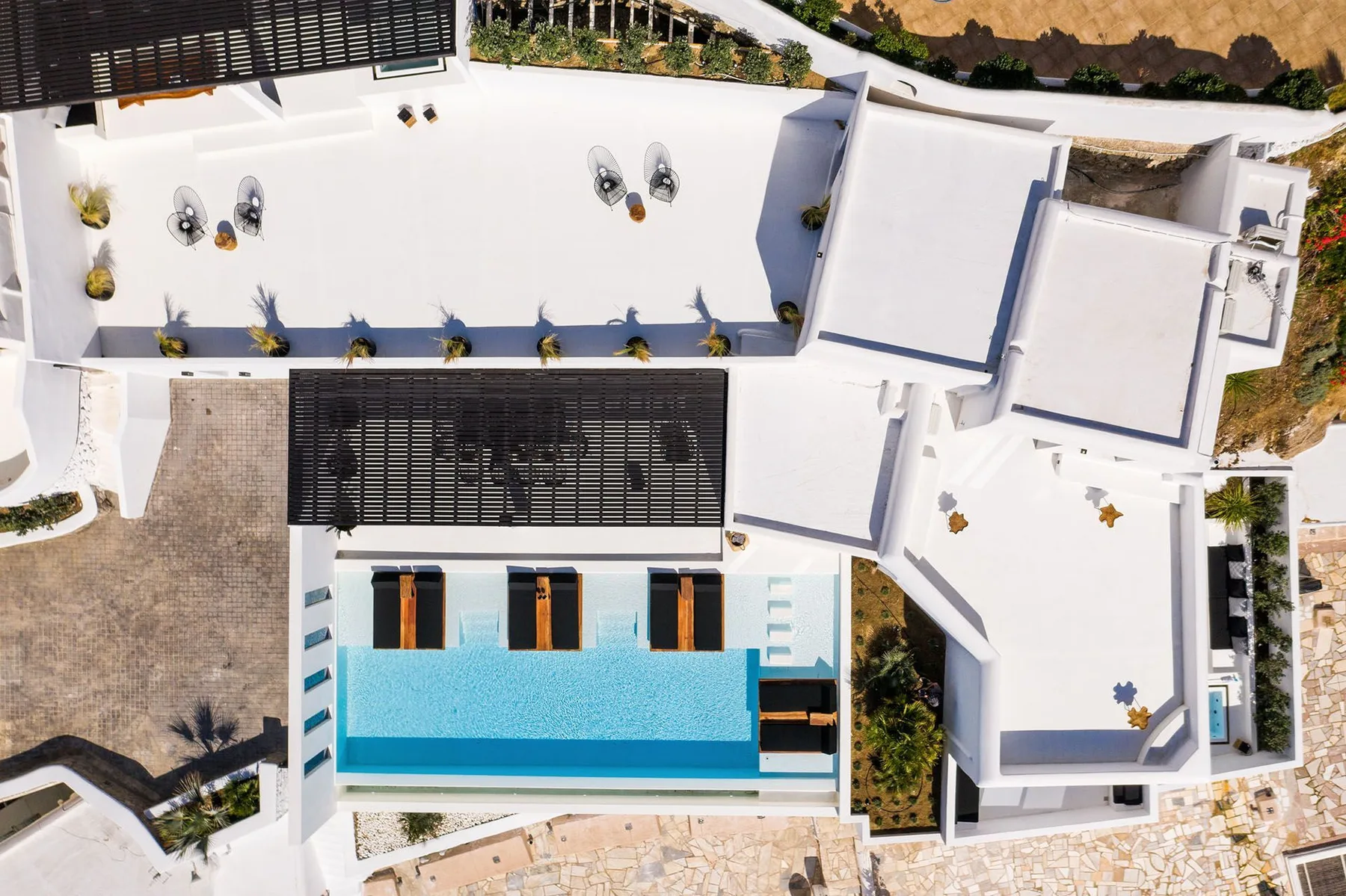 An overhead view of a swimming pool beside white buildings and paved walkways.