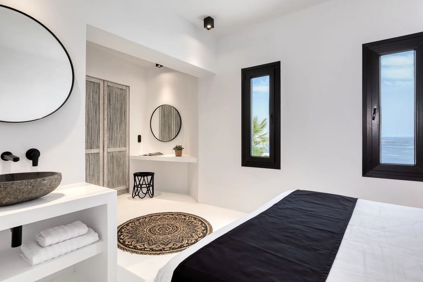 A bright bedroom with a bed, two windows, and an adjoining vanity area.