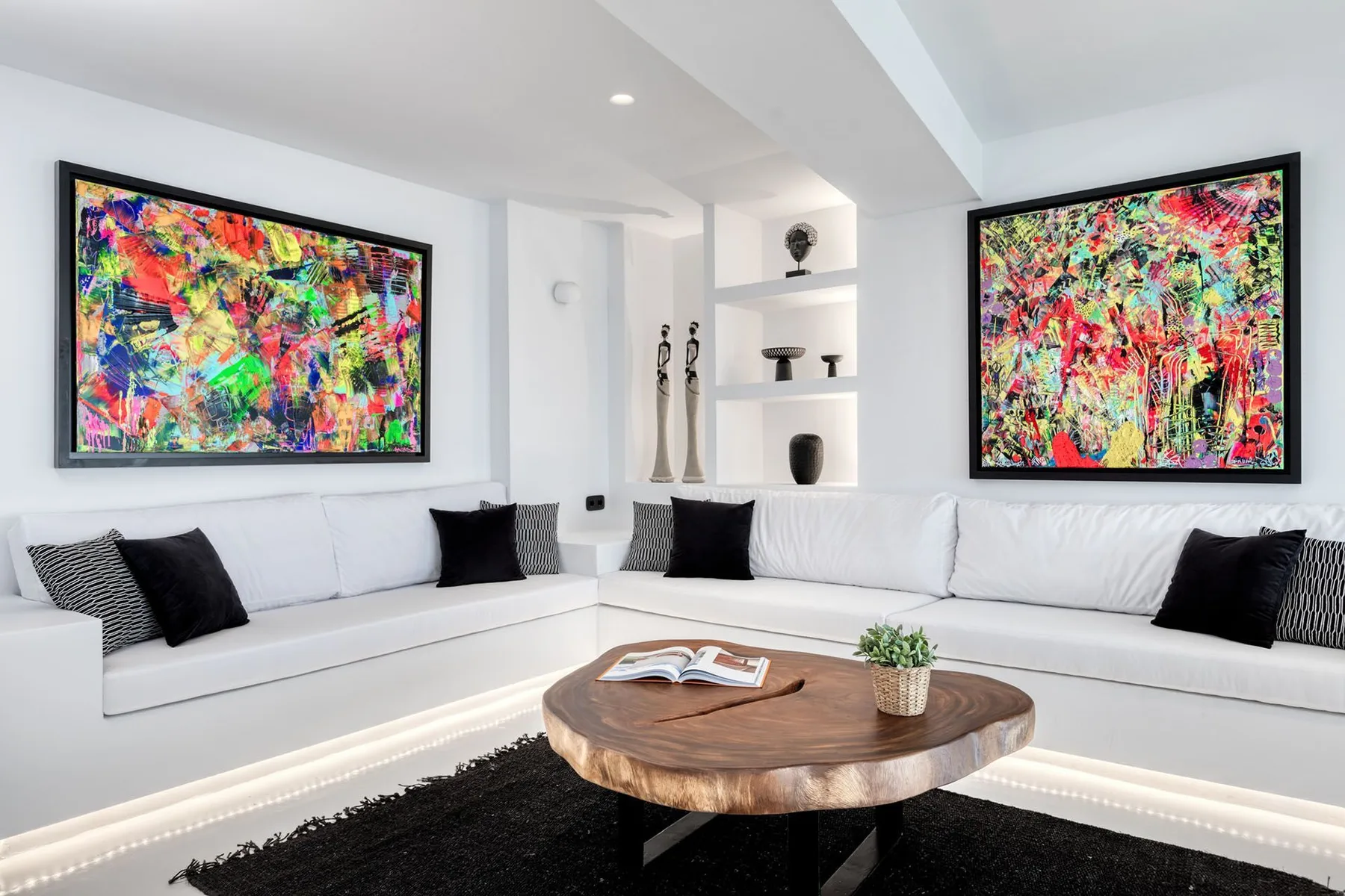 A bright living room with white sectional seating and colorful abstract paintings.