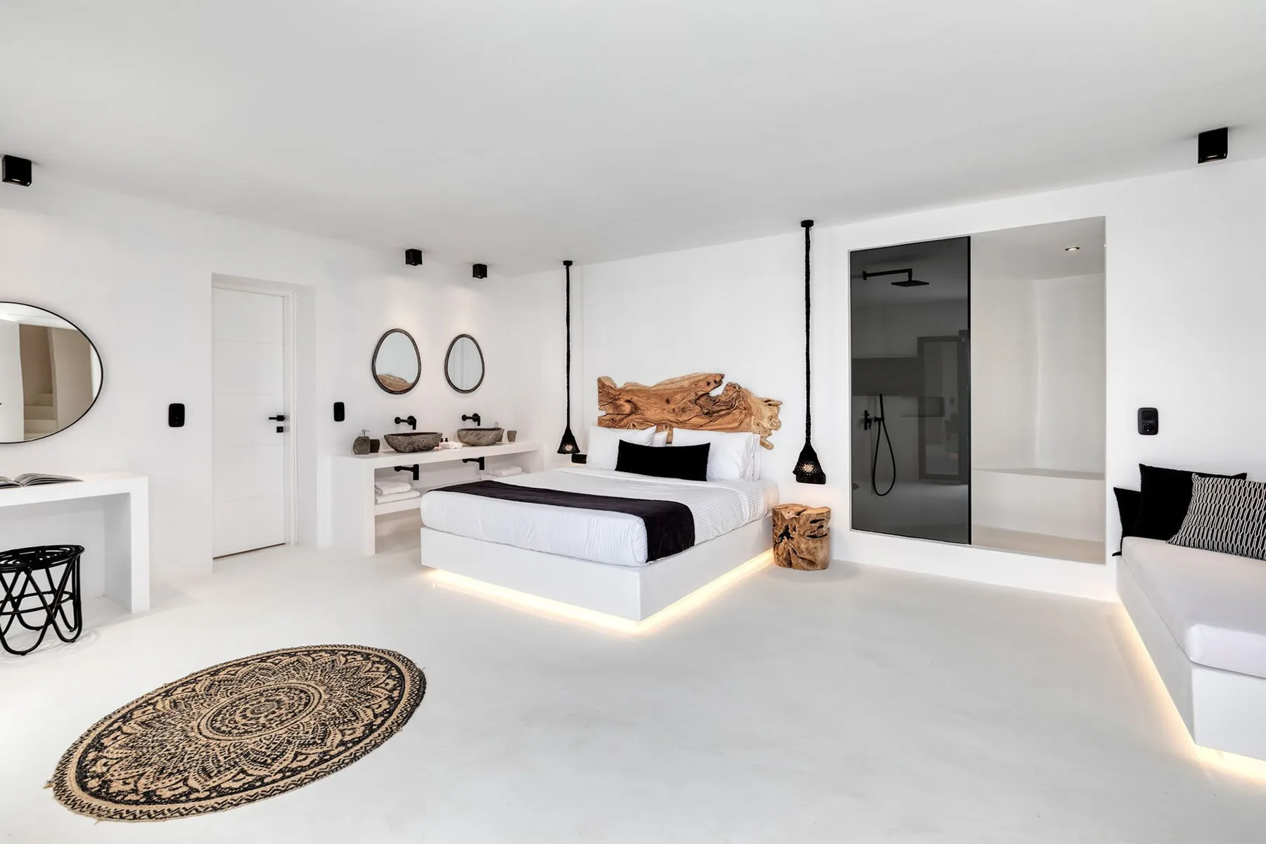 A bright bedroom with a large bed, vanity area, and glass-enclosed shower.