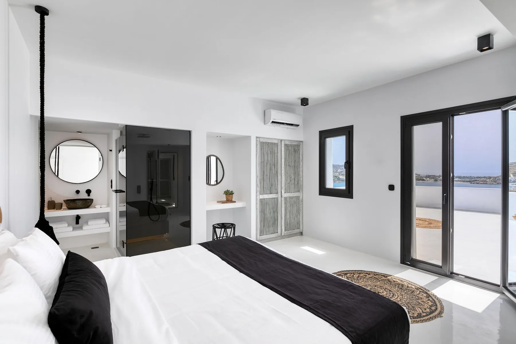 A bright bedroom with a large bed, mirrored closet doors, and sliding glass doors.