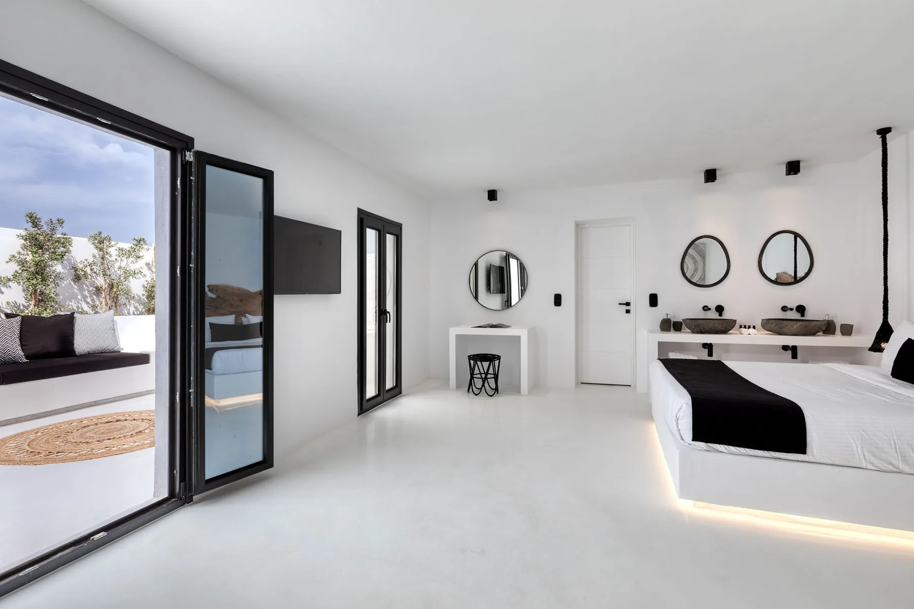 A bright bedroom with two beds, round mirrors, and an open glass door to a terrace.