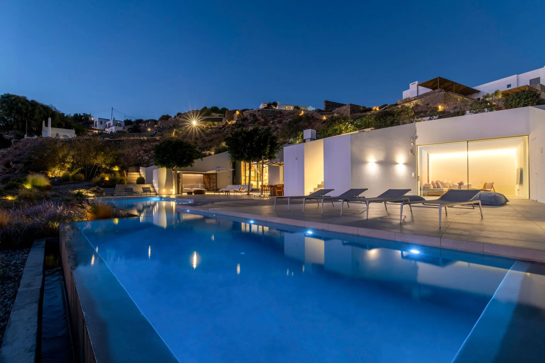 An illuminated outdoor swimming pool beside a modern building at dusk.