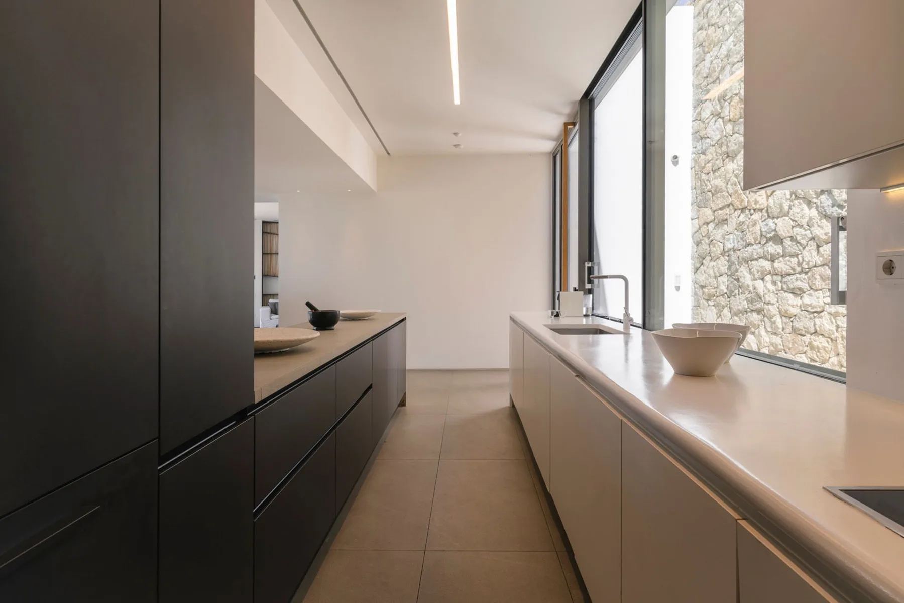 A modern kitchen with dark cabinetry, a long counter, and a large window.