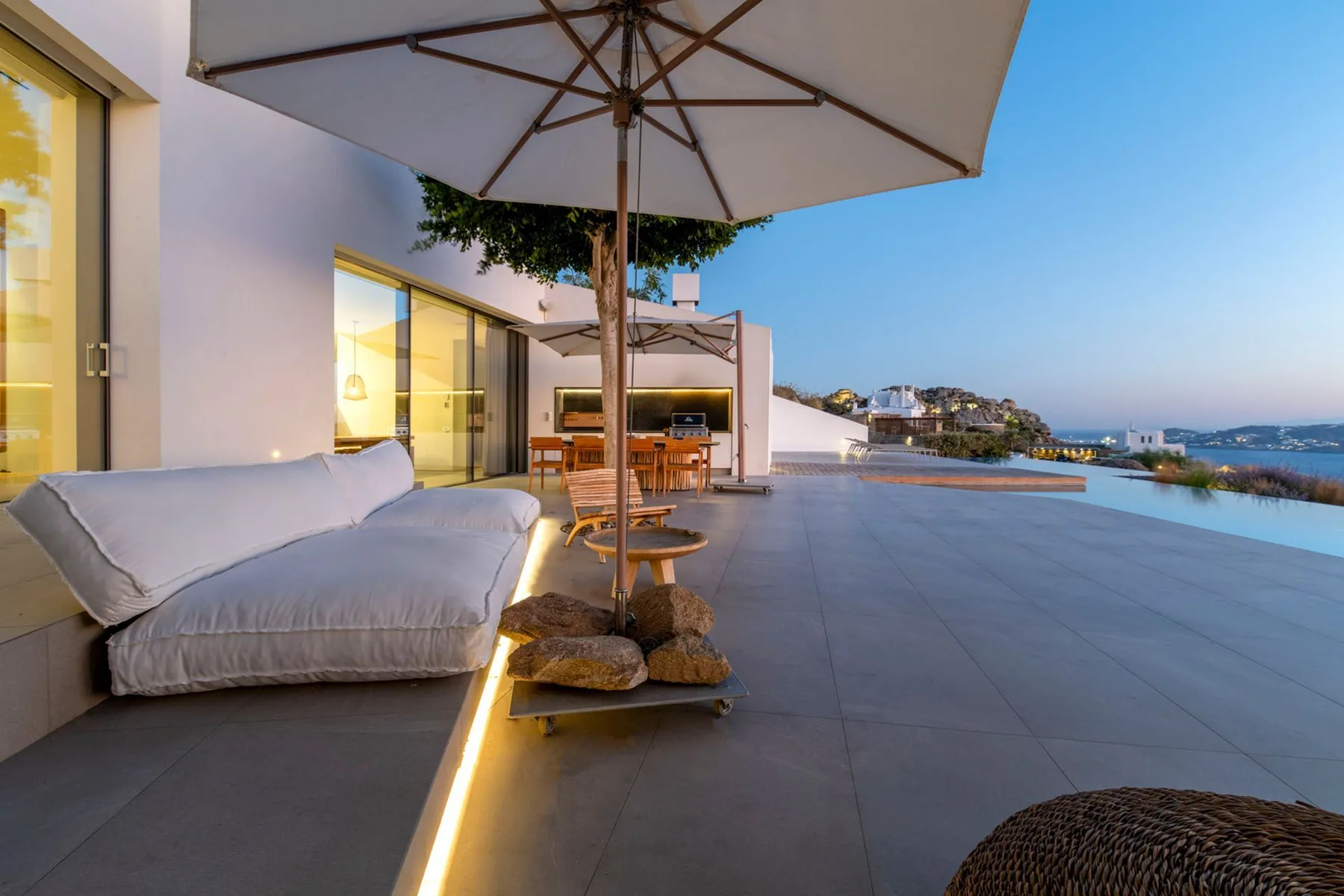 A spacious outdoor terrace with seating and a large sun umbrella overlooks the sea.