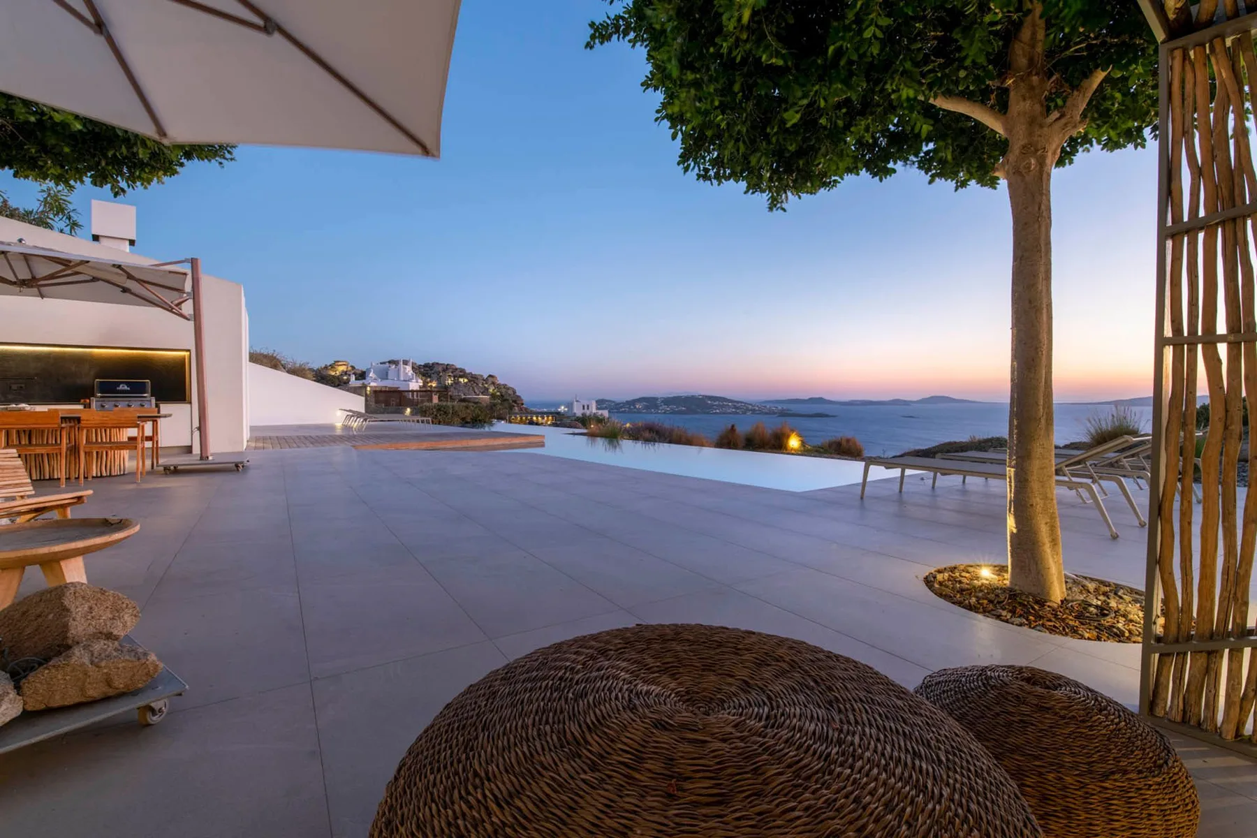 A seaside terrace at sunset with outdoor seating and a view of the water.