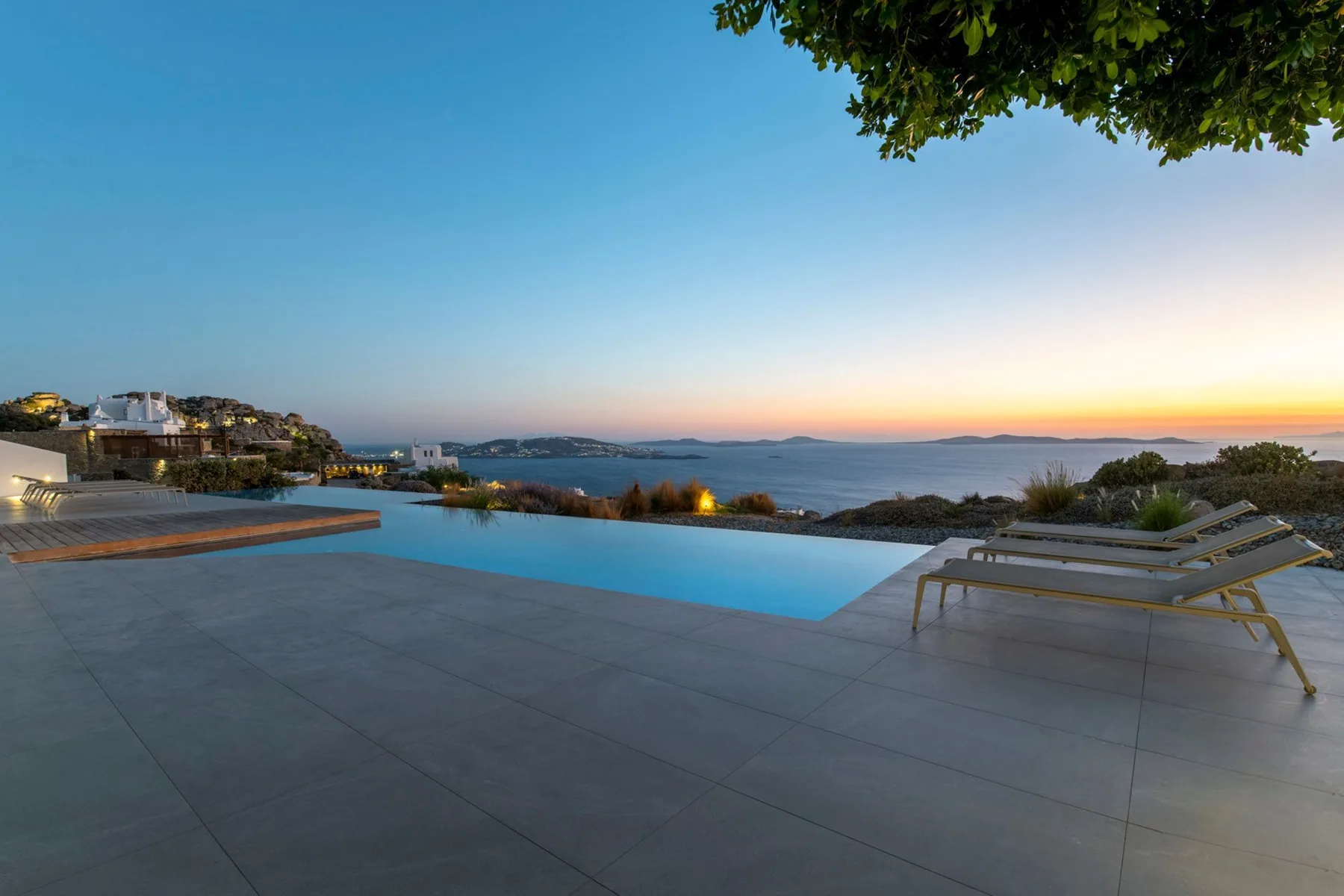 An outdoor swimming pool and paved terrace overlook the water at dusk.