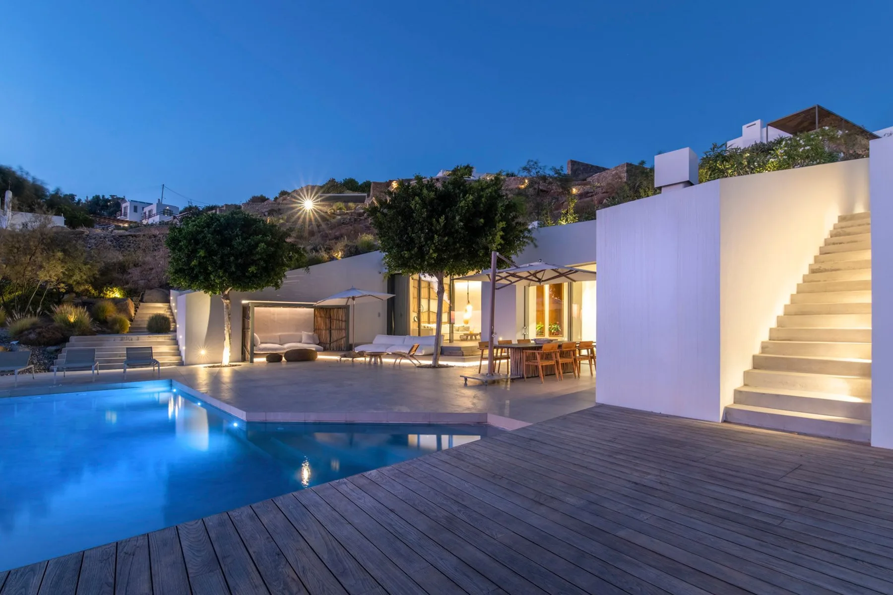 A poolside patio with outdoor seating, a wooden deck, and illuminated stairs.