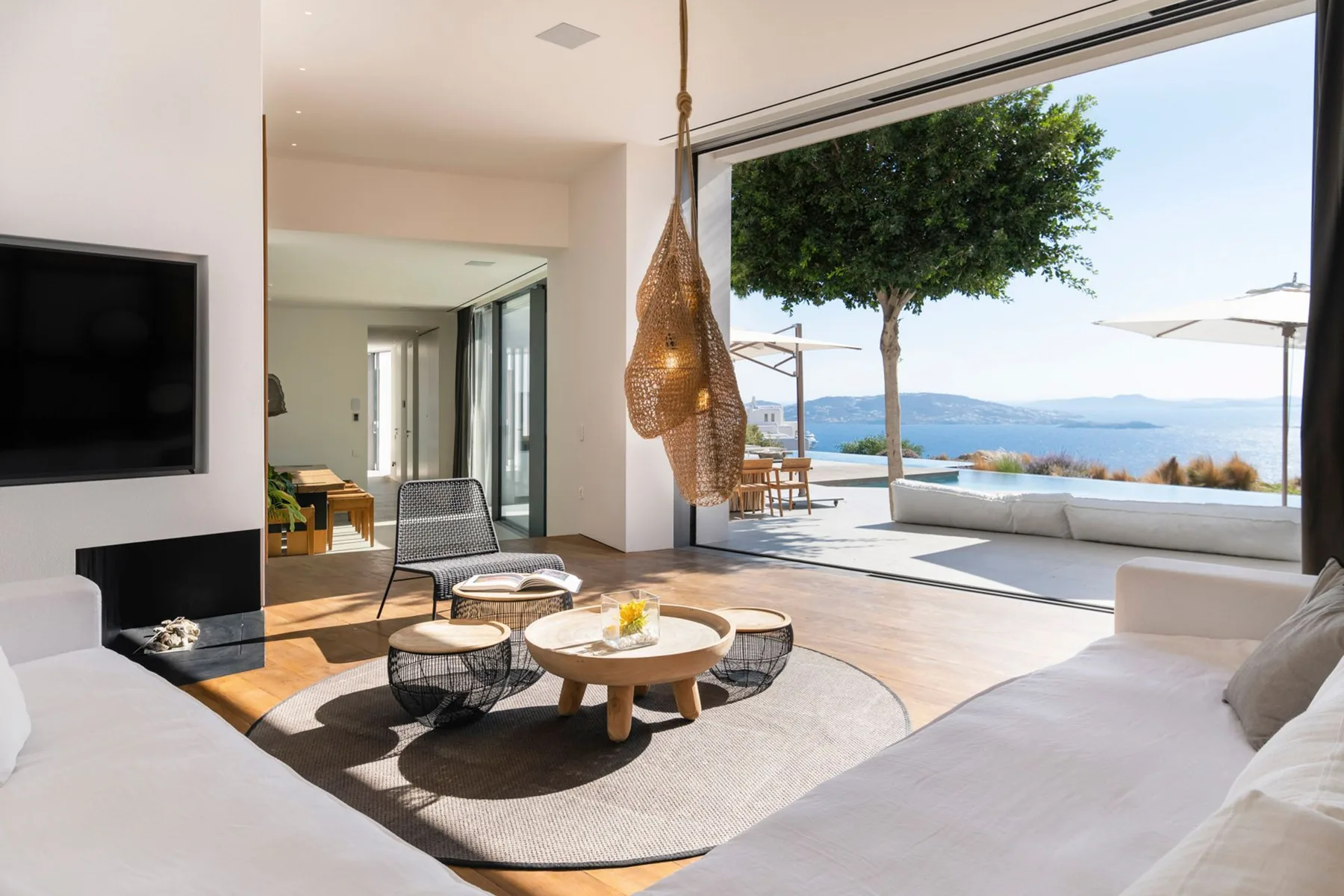 A bright living room opens onto a terrace with a tree and sea view.