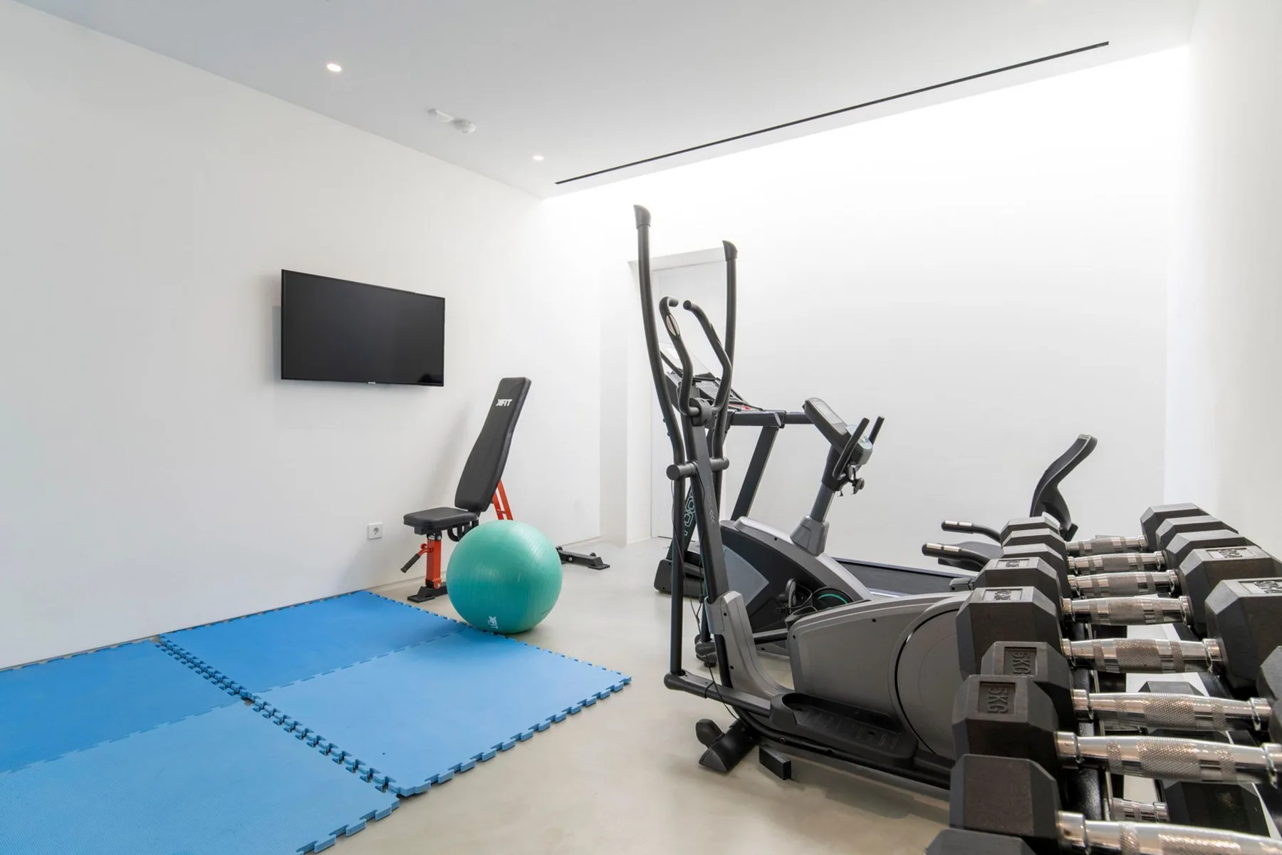 A gym with cardio equipment, dumbbells, and blue exercise mats.