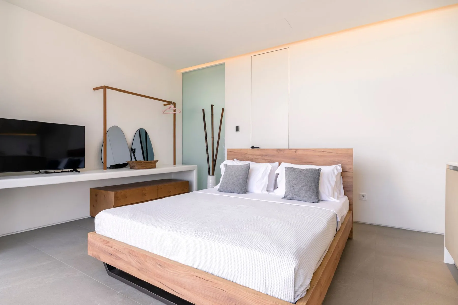 A bright bedroom with a bed, television, and wall-mounted shelving.