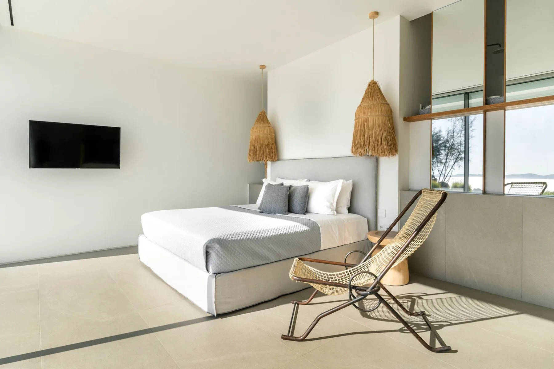 A bright bedroom with a white bed and a woven lounge chair.