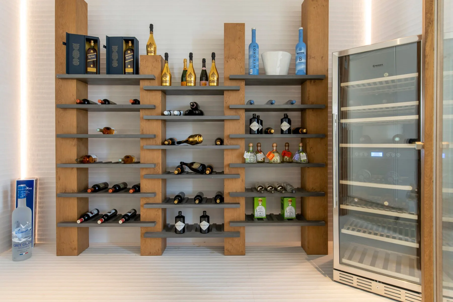 A wall-mounted wine display with bottles and a glass-front beverage cooler.