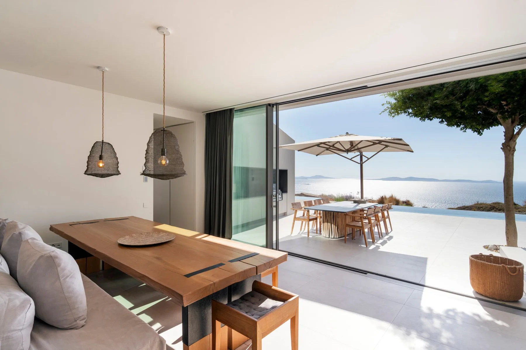A bright dining area opens onto a terrace with a table, umbrella, and sea view.
