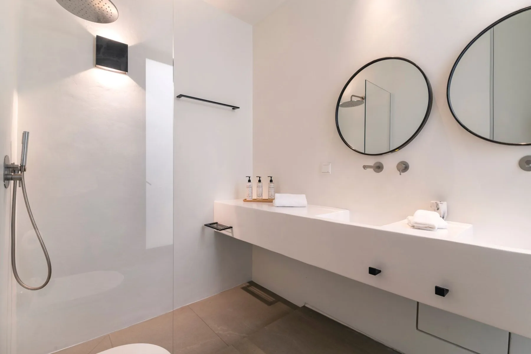 A bright bathroom with a walk-in shower and a long vanity beneath round mirrors.