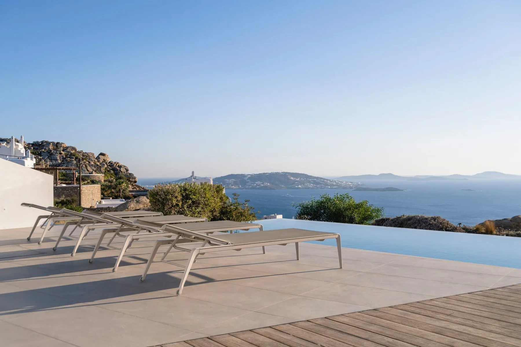 A poolside terrace overlooks the sea, with lounge chairs beside the water.