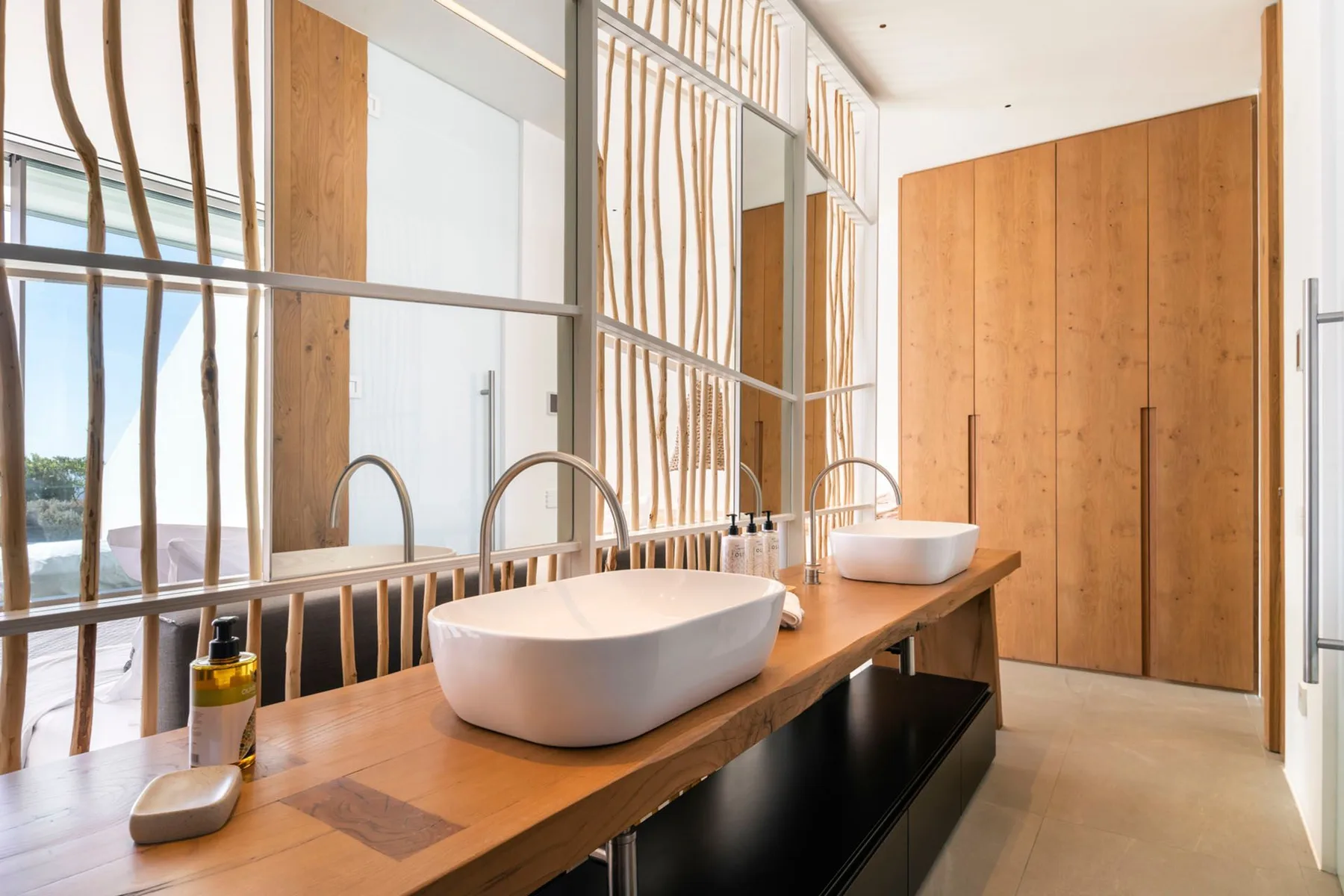 A bright bathroom vanity has vessel sinks set along a long wooden counter.