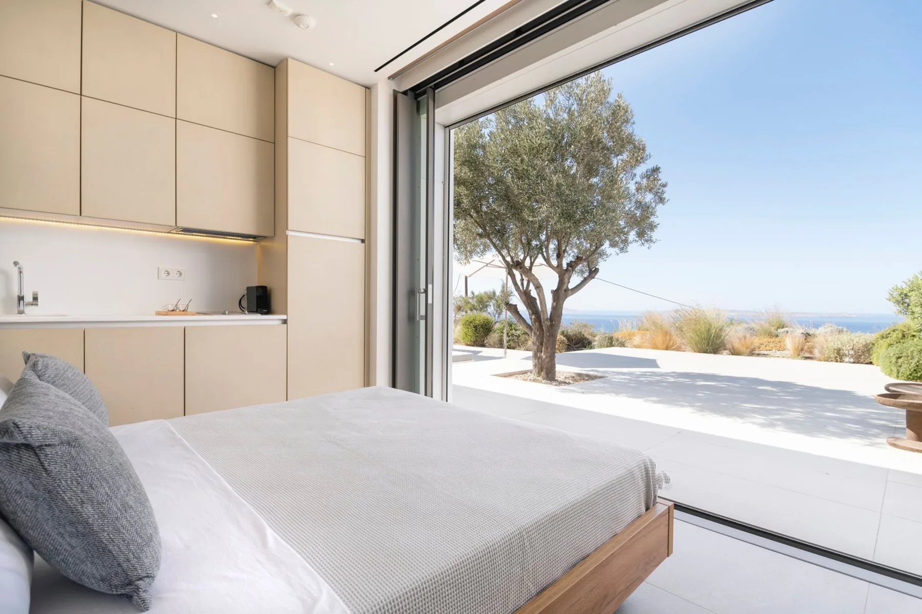 A bedroom with a bed beside a kitchenette and a large open window.