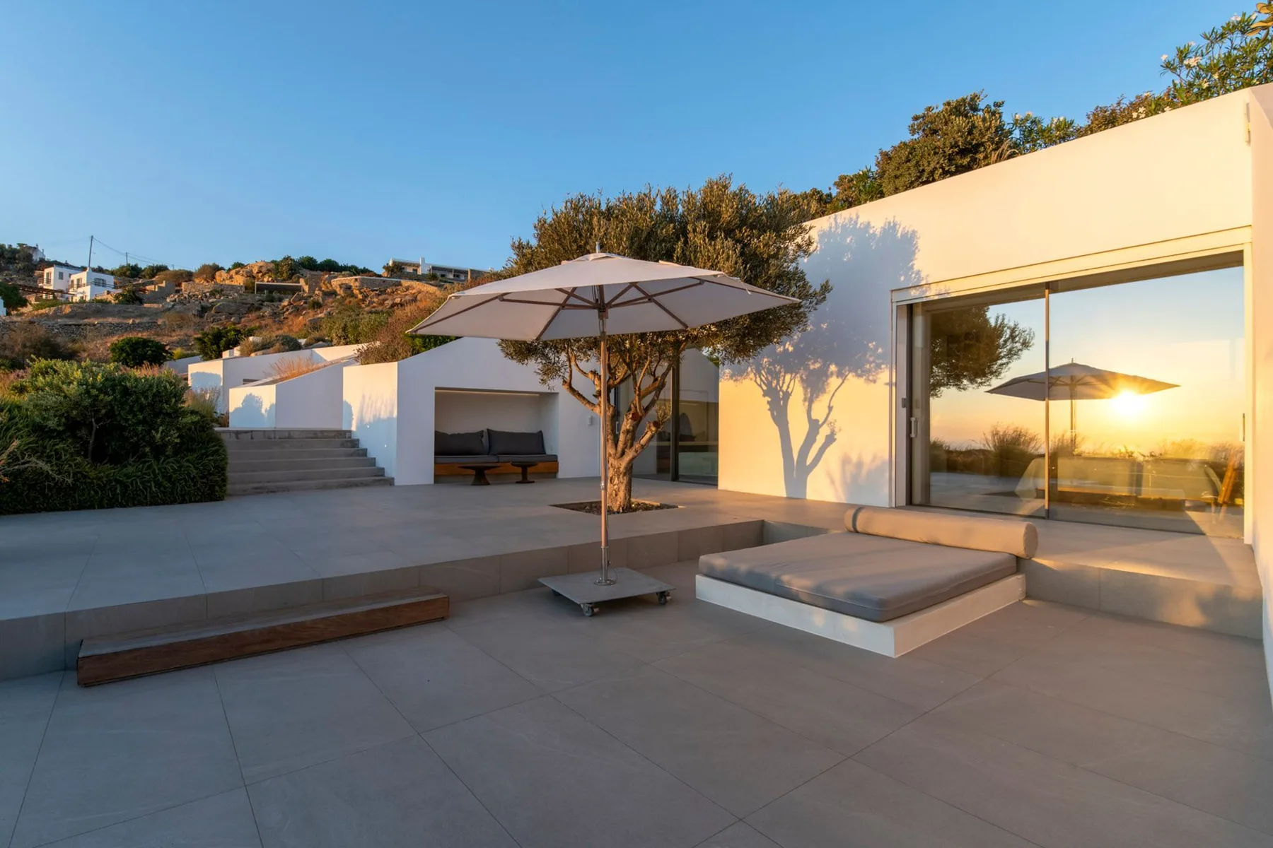 A modern outdoor patio has a shade umbrella, built-in seating, and a large glass wall.