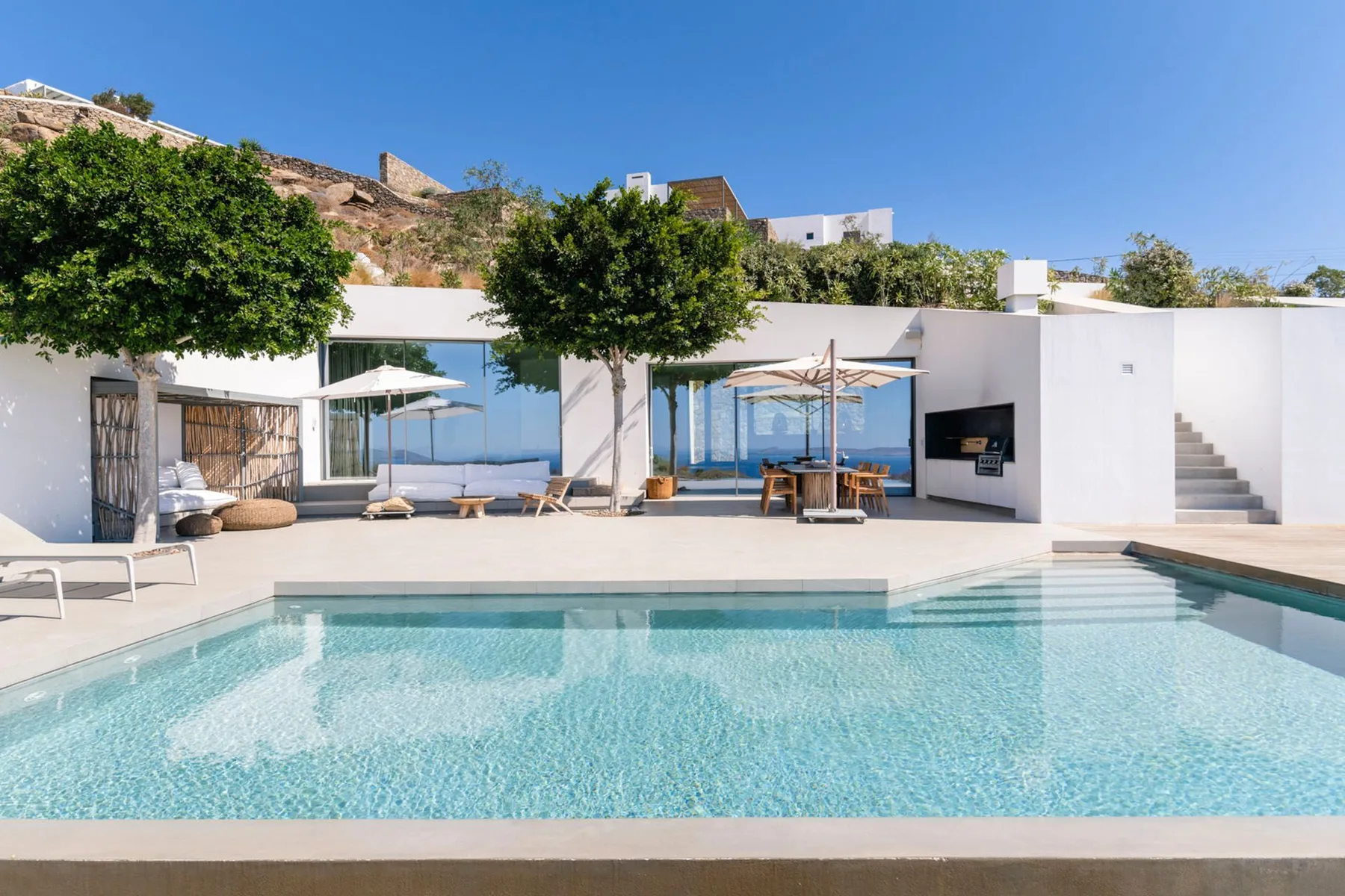 A swimming pool in front of a modern white building with outdoor seating.