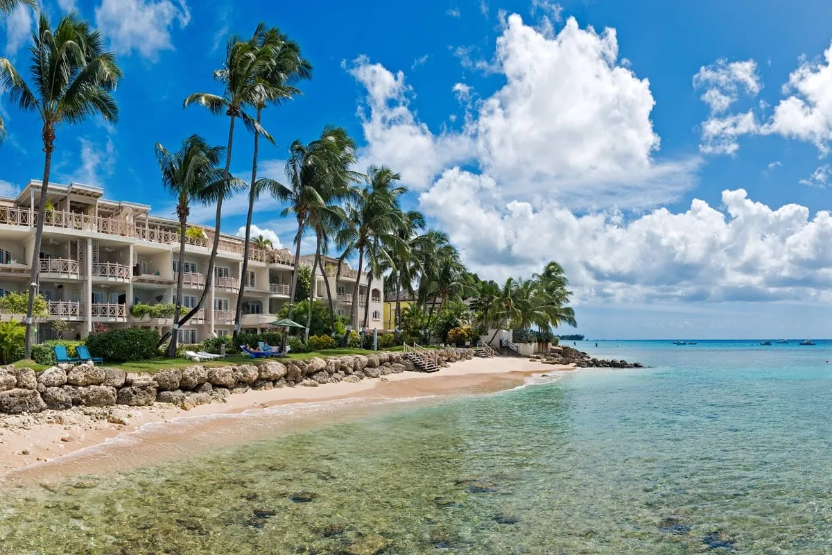 Shared amenity: A tropical beach beside a palm-lined resort, with clear water along the shore.