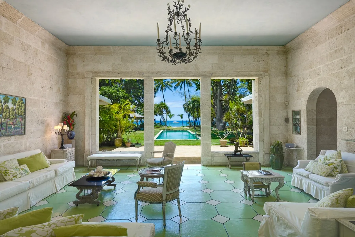 Una sala luminosa se abre a un jardín y una piscina a través de tres grandes ventanas.