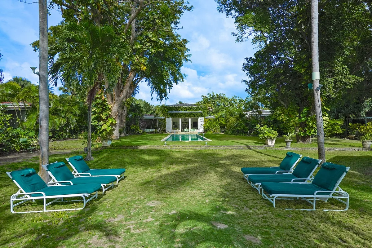 Un jardín con césped, asientos reclinables, árboles y una piscina pequeña.