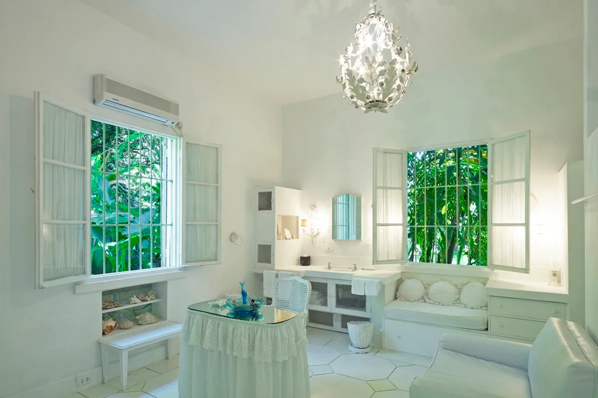 Una luminosa zona de estar blanca con ventanas abiertas que dan a la vegetación.