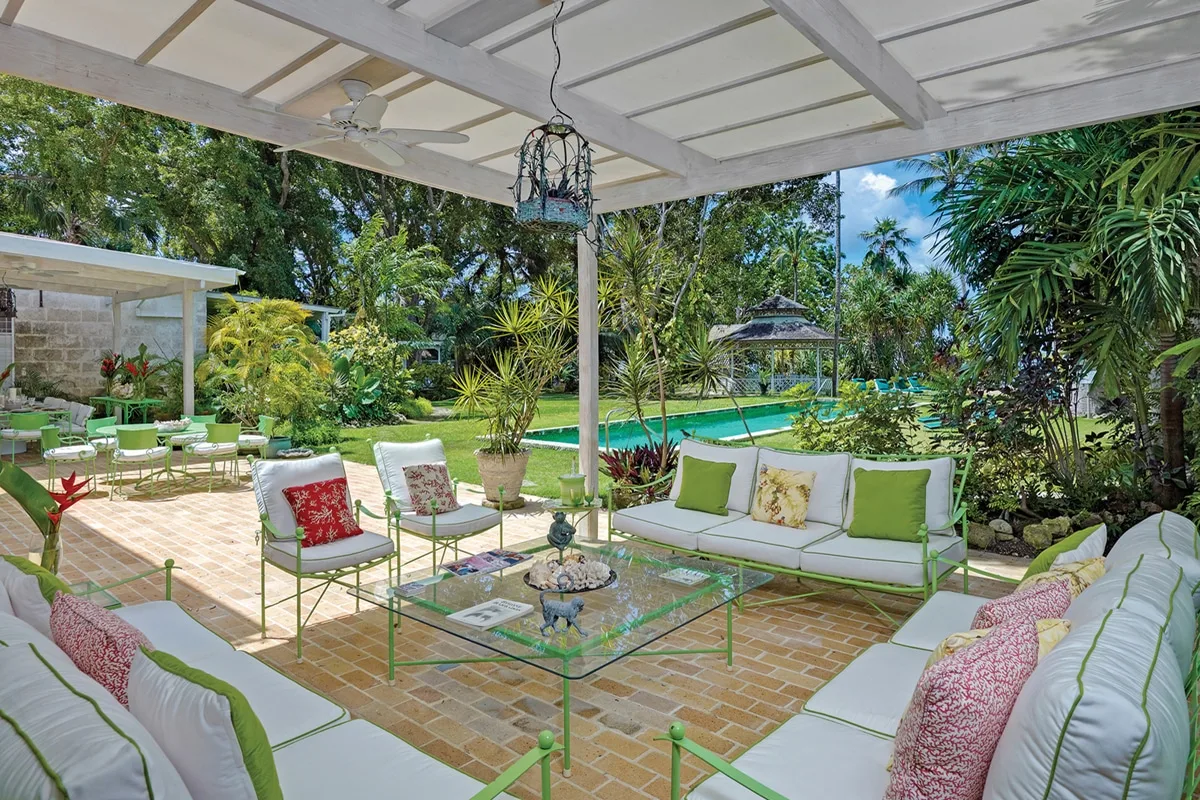Una zona de estar al aire libre y cubierta da a una piscina y un jardín tropical.