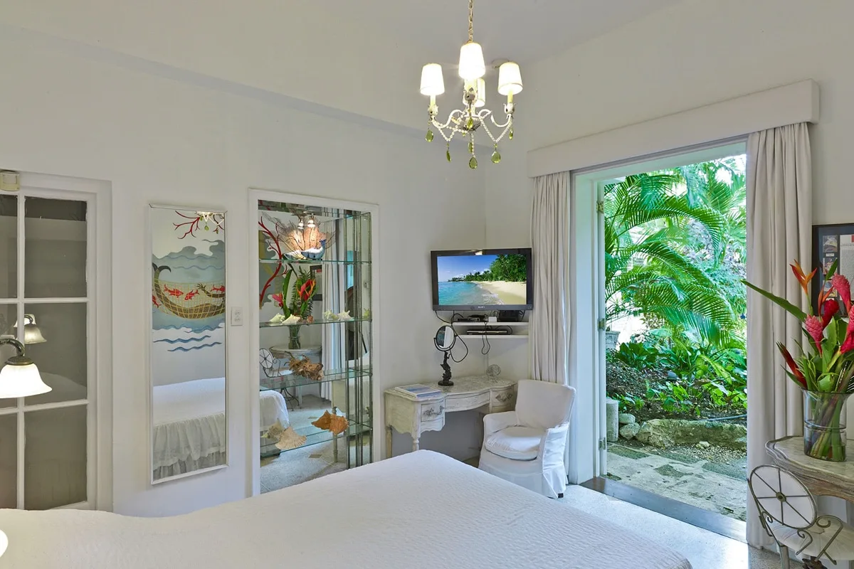 Un dormitorio luminoso con una cama, un televisor y vistas al jardín a través de puertas de vidrio abiertas.