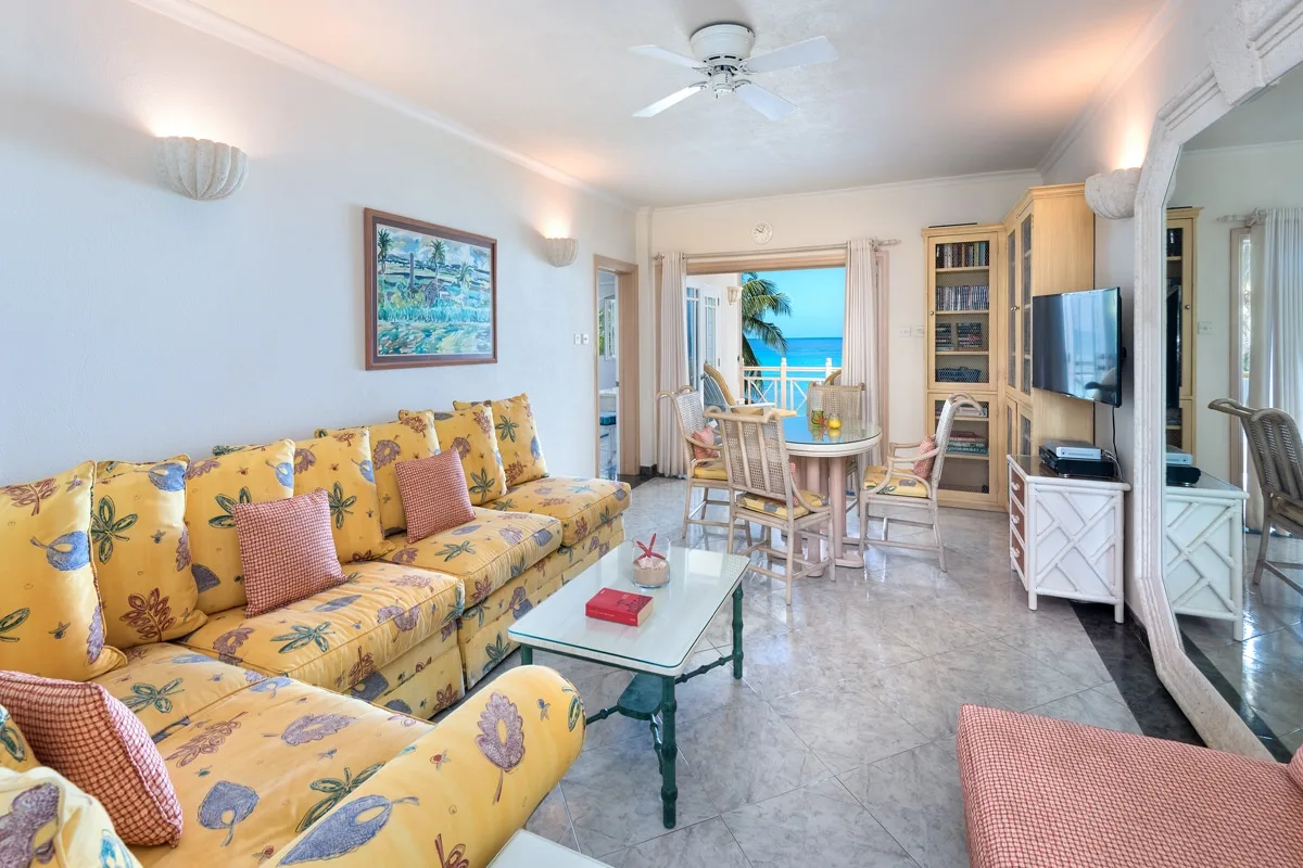 A bright living room has floral seating and a dining area beside a balcony.