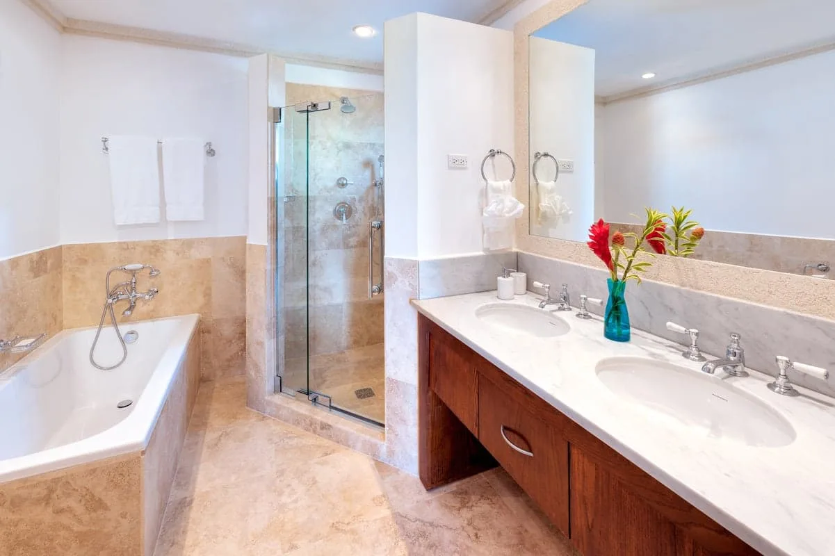 Un baño luminoso con bañera, ducha de vidrio y tocador con dos lavabos.