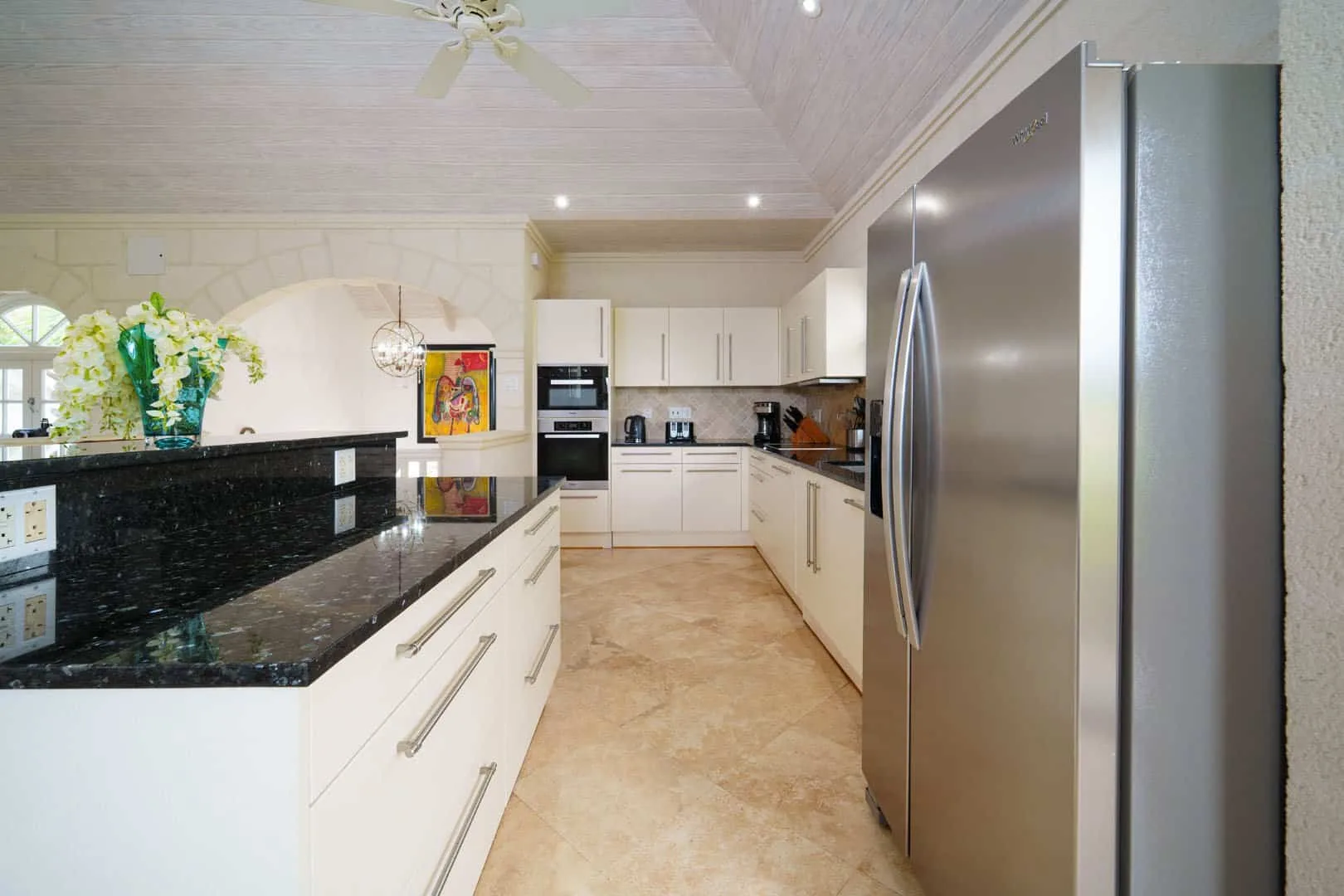 Una cocina luminosa con gabinetes blancos, encimeras oscuras y un refrigerador de acero inoxidable.