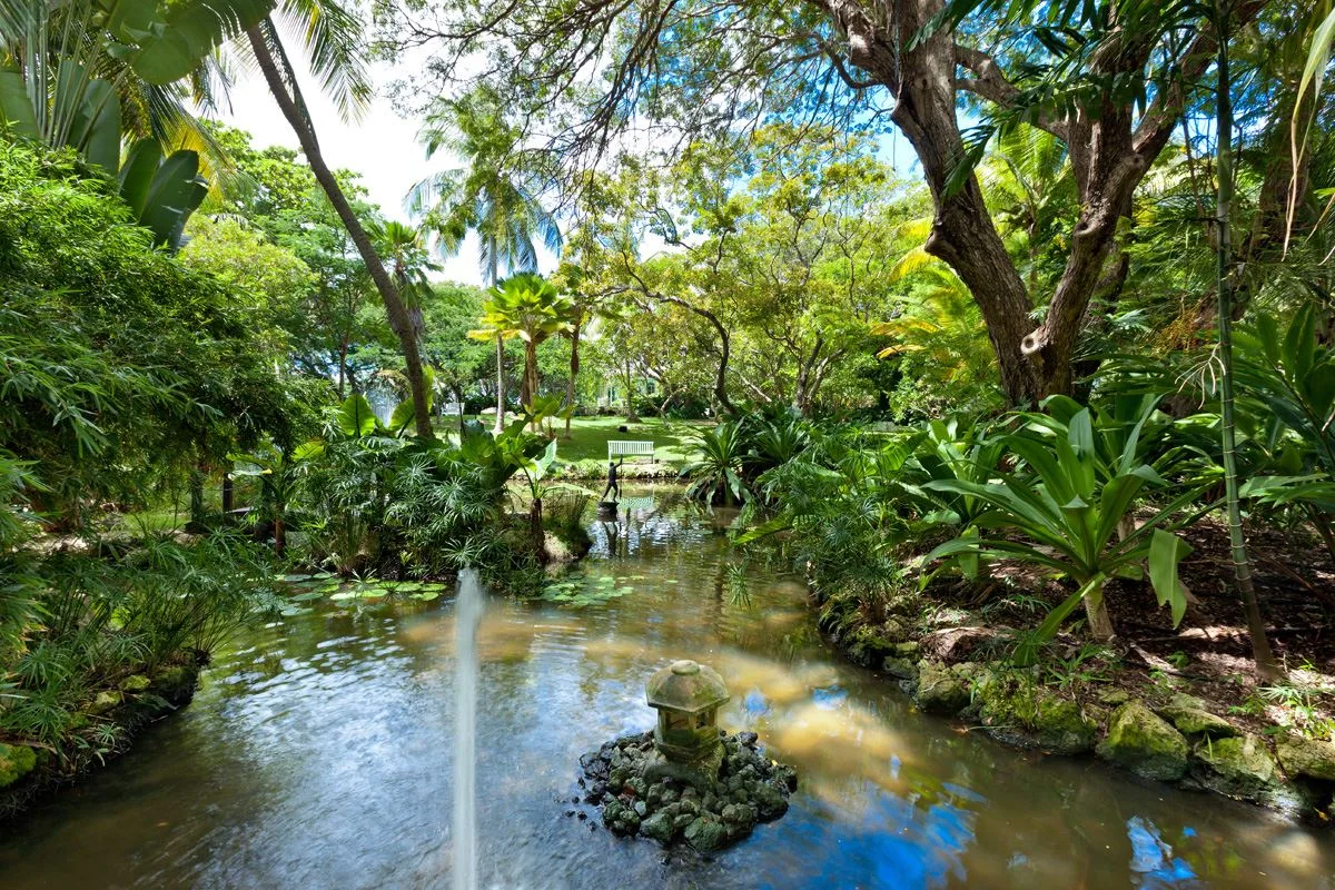 A lush garden surrounds a shallow stream, with a small fountain in the foreground.