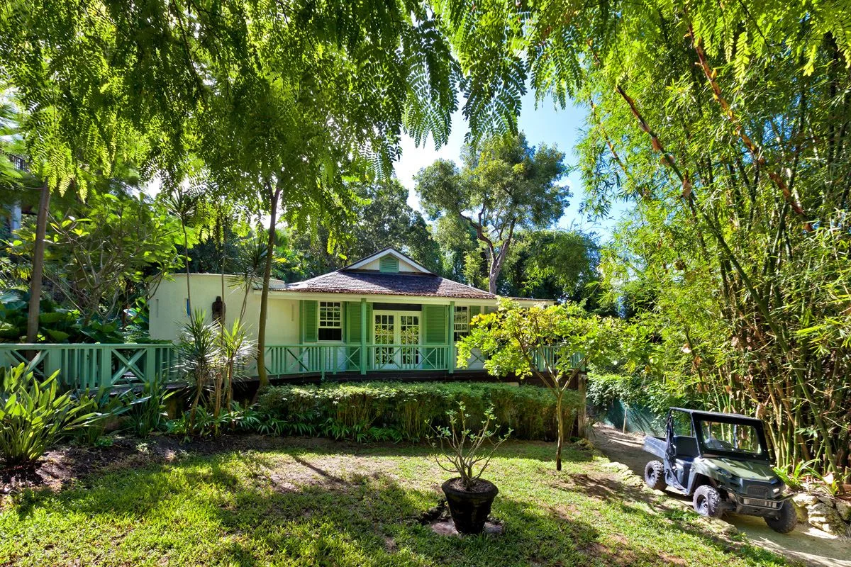 A green cottage sits among leafy trees beside a garden path.